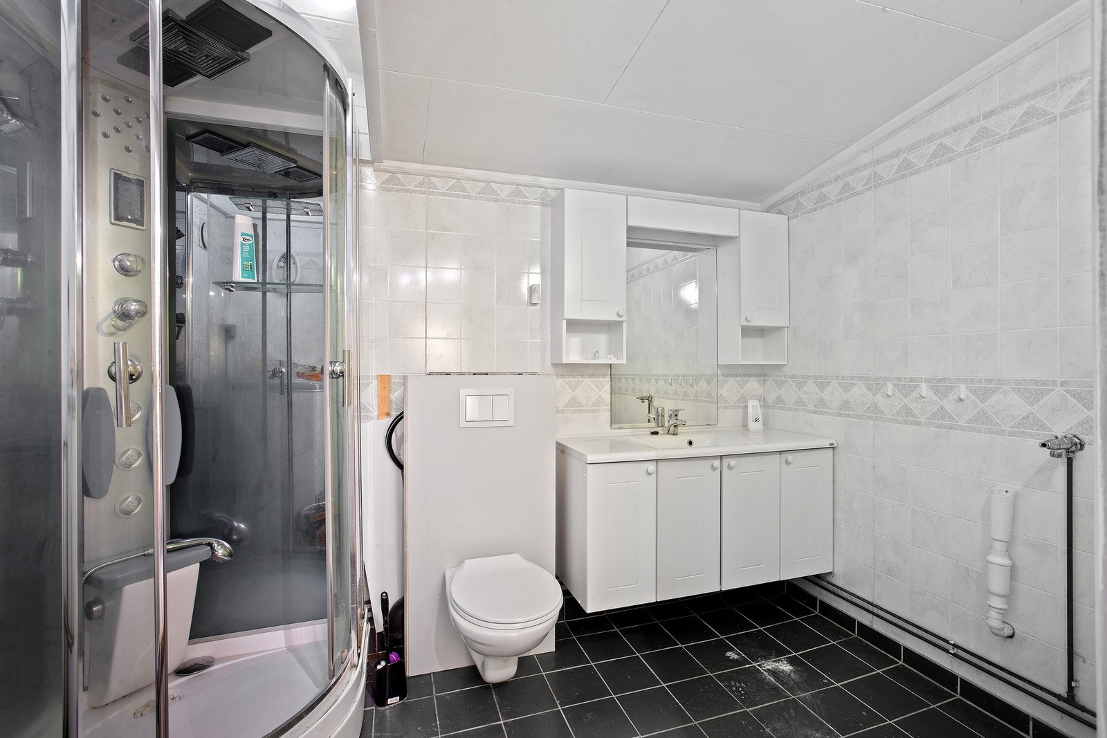 Badet har lys innredning med nedfelt servant og skap under, overskap og speil over, dusjkabinett og toalett. Galleribilde