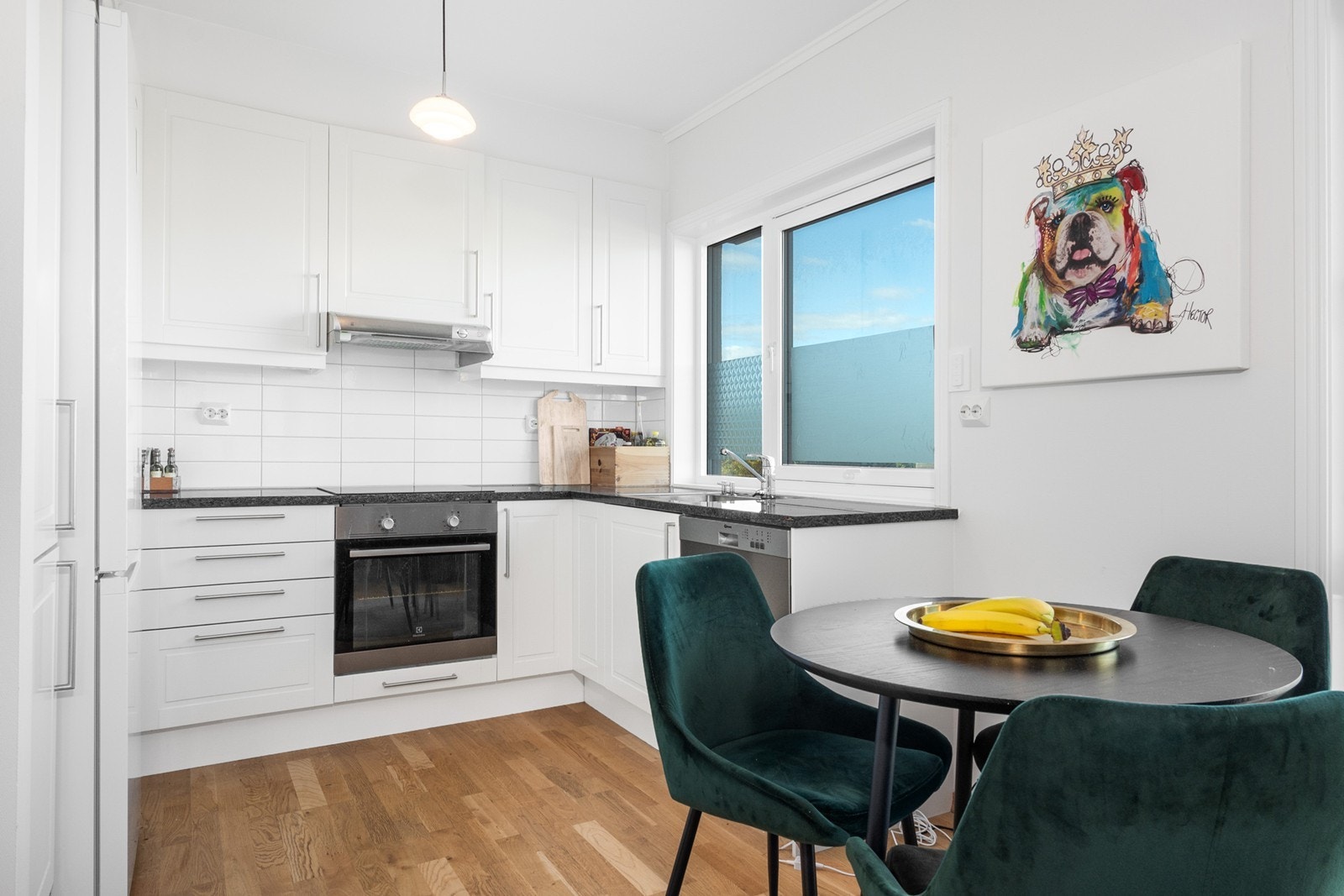 Kjøkkenet fra byggeår har alt man trenger plassert i en praktisk L-form. Innredningen har hvite, profilerte fronter og hvit laminat benkeplate med nedfelt kum. Galleribilde