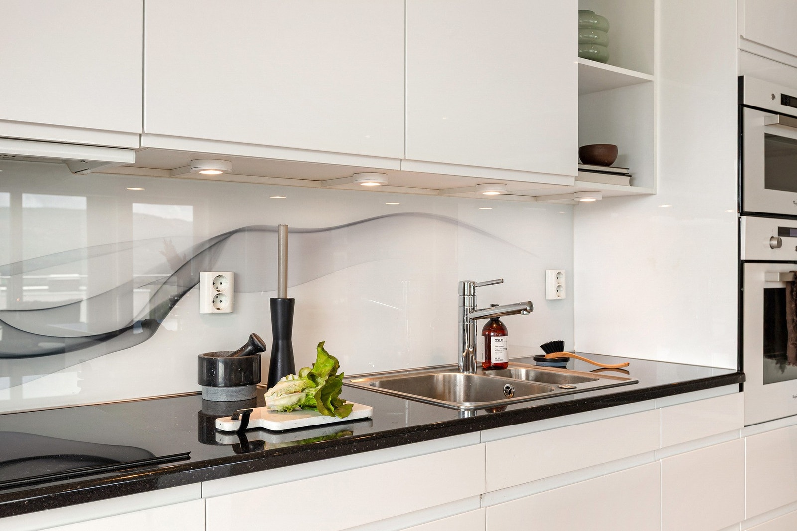 Nedfelt platetopp i kjøkkeninnredningen. Det er montert glassplate på veggen mellom benkplate og overskap. Downlights med dimmerløsning Galleribilde
