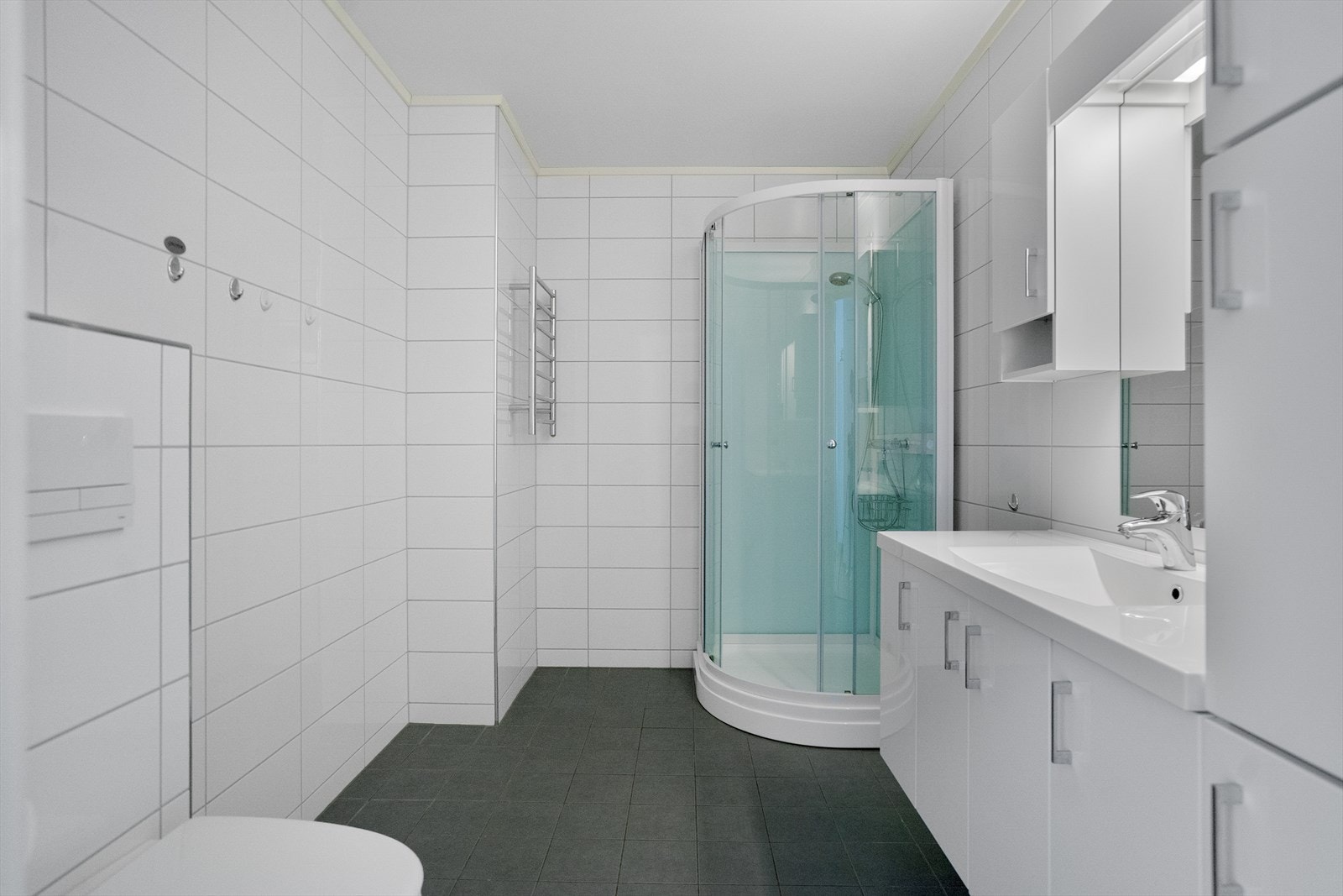 Badet er innredet med vegghengt toalett, dusjkabinett og stilrene overflater Galleribilde