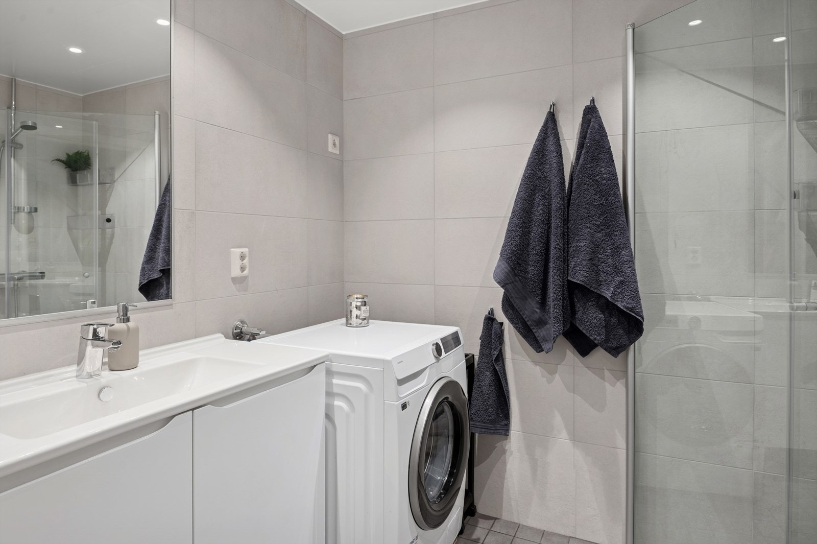 Baderommet har hvit glatt innredning med med nedfelt servant, veggmontert toalett, dusjvegger/hjørne og opplegg for vaskemaskin. Galleribilde