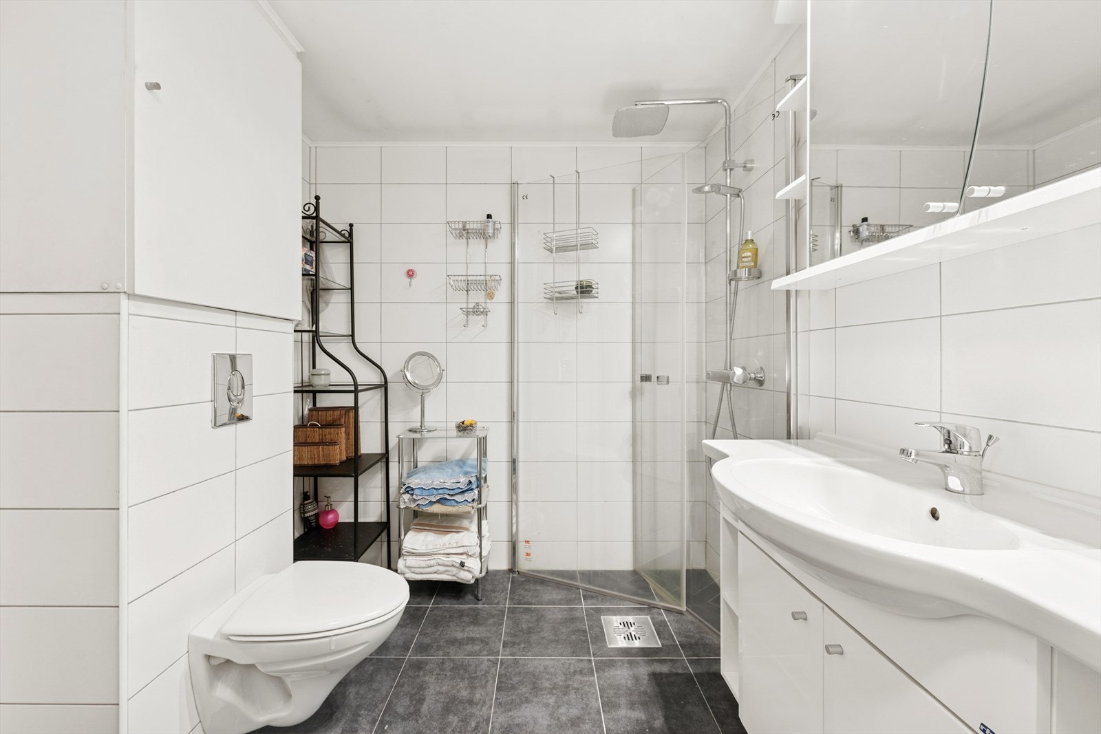 Badet er utstyrt med vegghengt toalett, svingbare dusjdører, baderomsinnredning med servant og veggskap. Galleribilde