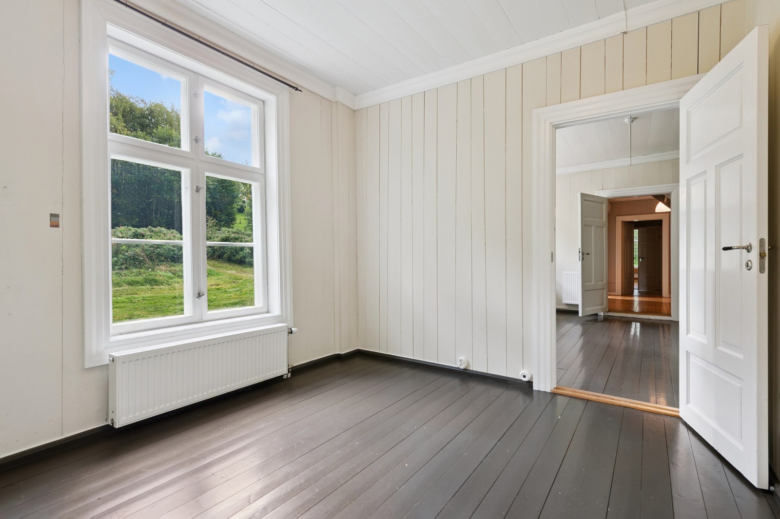 Et lyst rom med panel på veggene og utsikt mot eiendommens grøntområder. Galleribilde