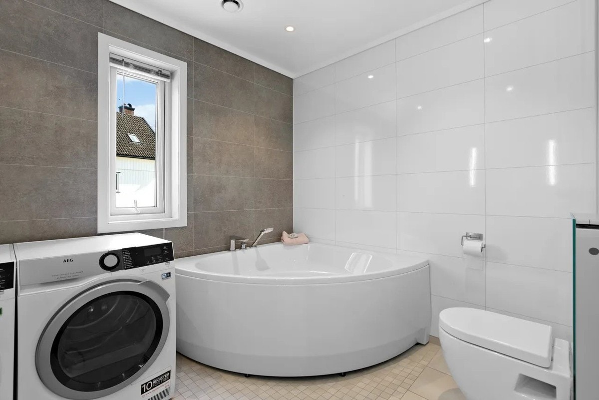 Et stilfullt bad med gulv- og veggfliser som gir rommet en behagelig atmosfære. Her finner du badekar, toalett, nedfelt servant, opplegg for vaskemaskin, gulvvarme og downlights i taket. Galleribilde