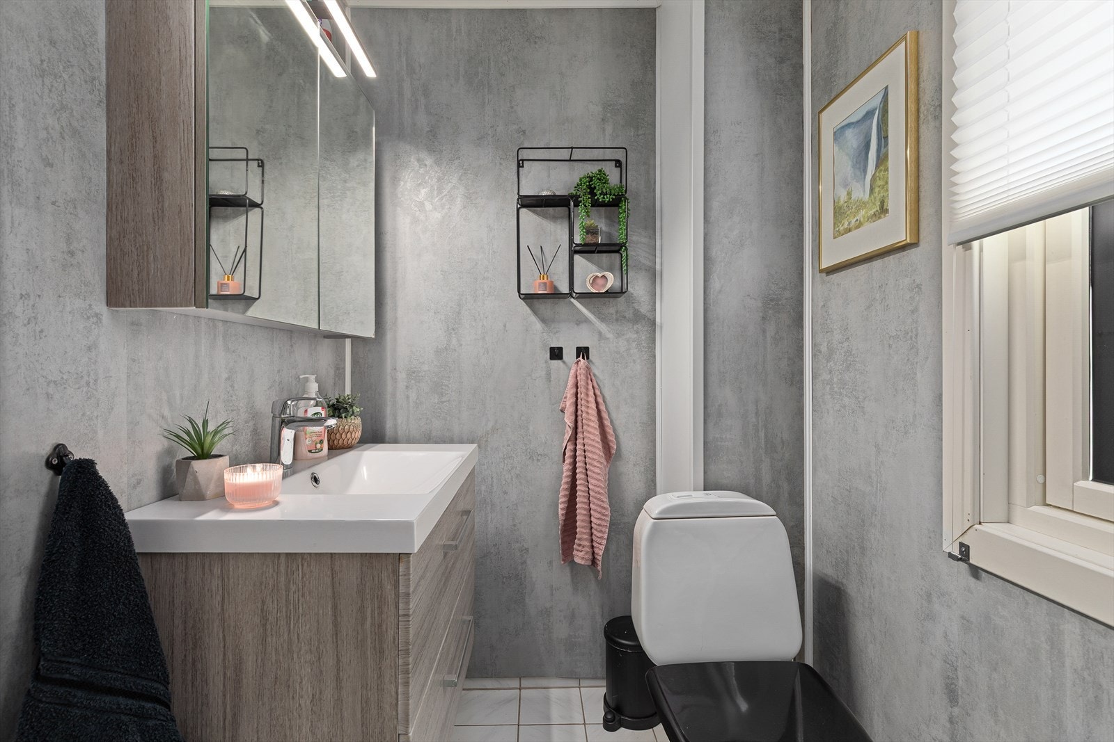 Bad med flisar på golv, og baderomsplatar på vegg. Frittståande toalett og moderne innreiing med servant, og speilskåp. Galleribilde