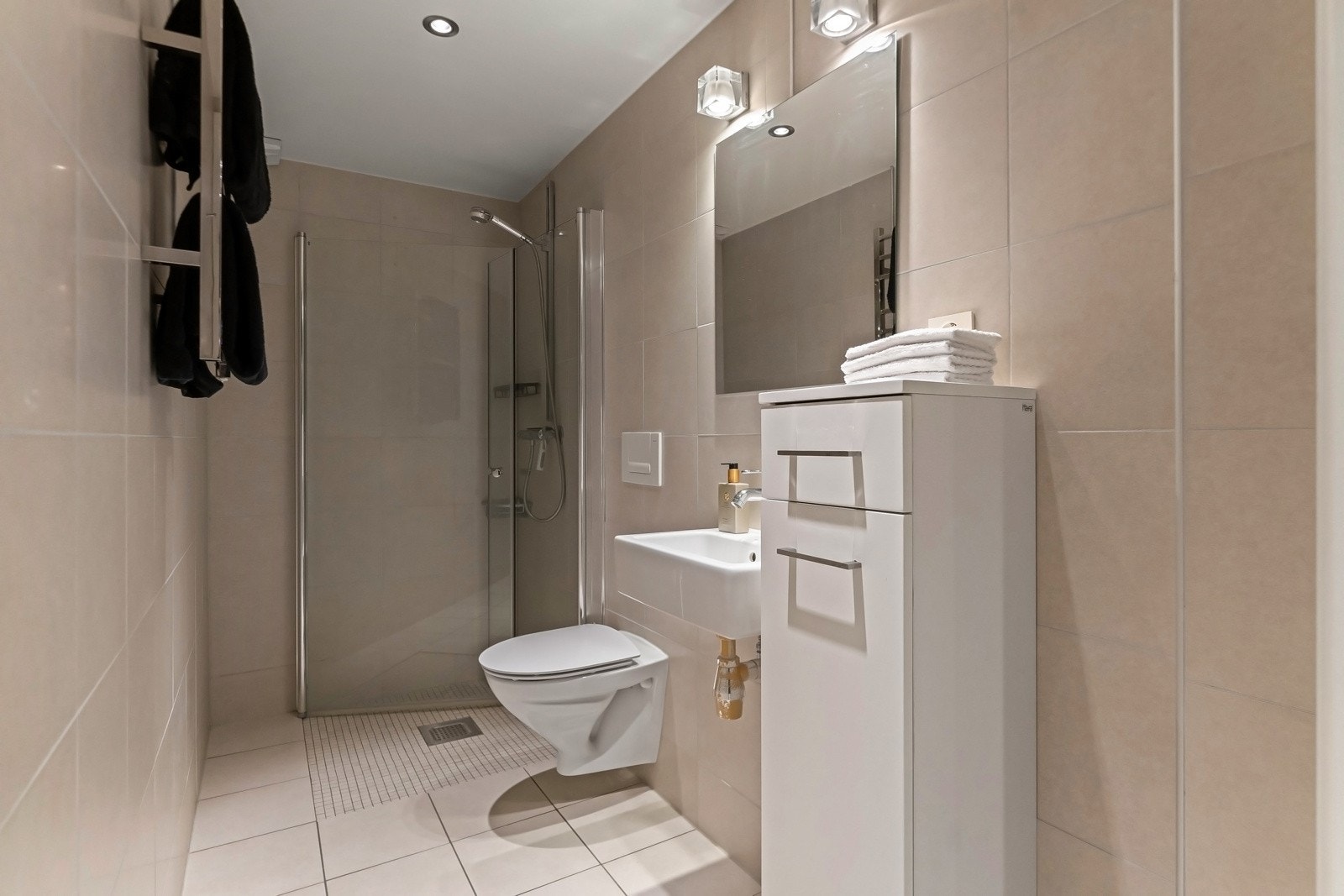 Det andre badet har lysbeige fliser på gulv og vegger, matchende mosaikk på gulvet i dusjen, downlights og gulvvarme. Galleribilde