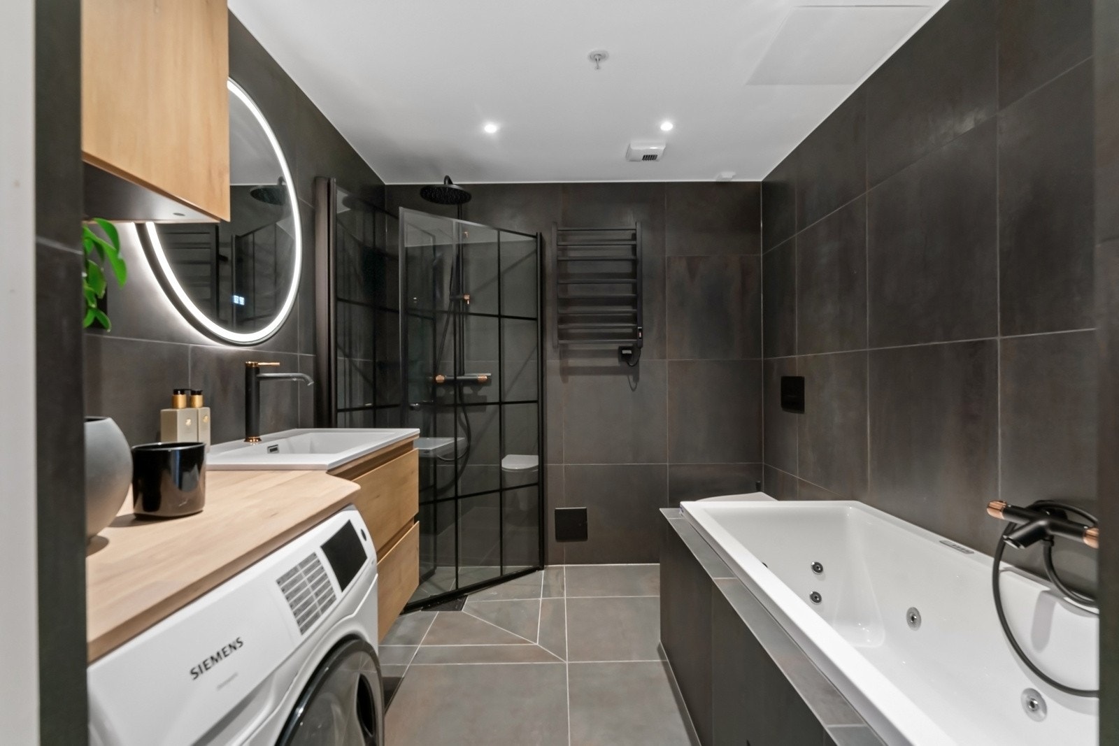 Dette badet ligger tilknyttet hovedsoverommet via garderoberommet. Her er det valgt mørke storformatfliser på gulv og vegger, samt sorte armaturer med kobberdetaljer som gir et elegant og eksklusivt inntrykk. Galleribilde