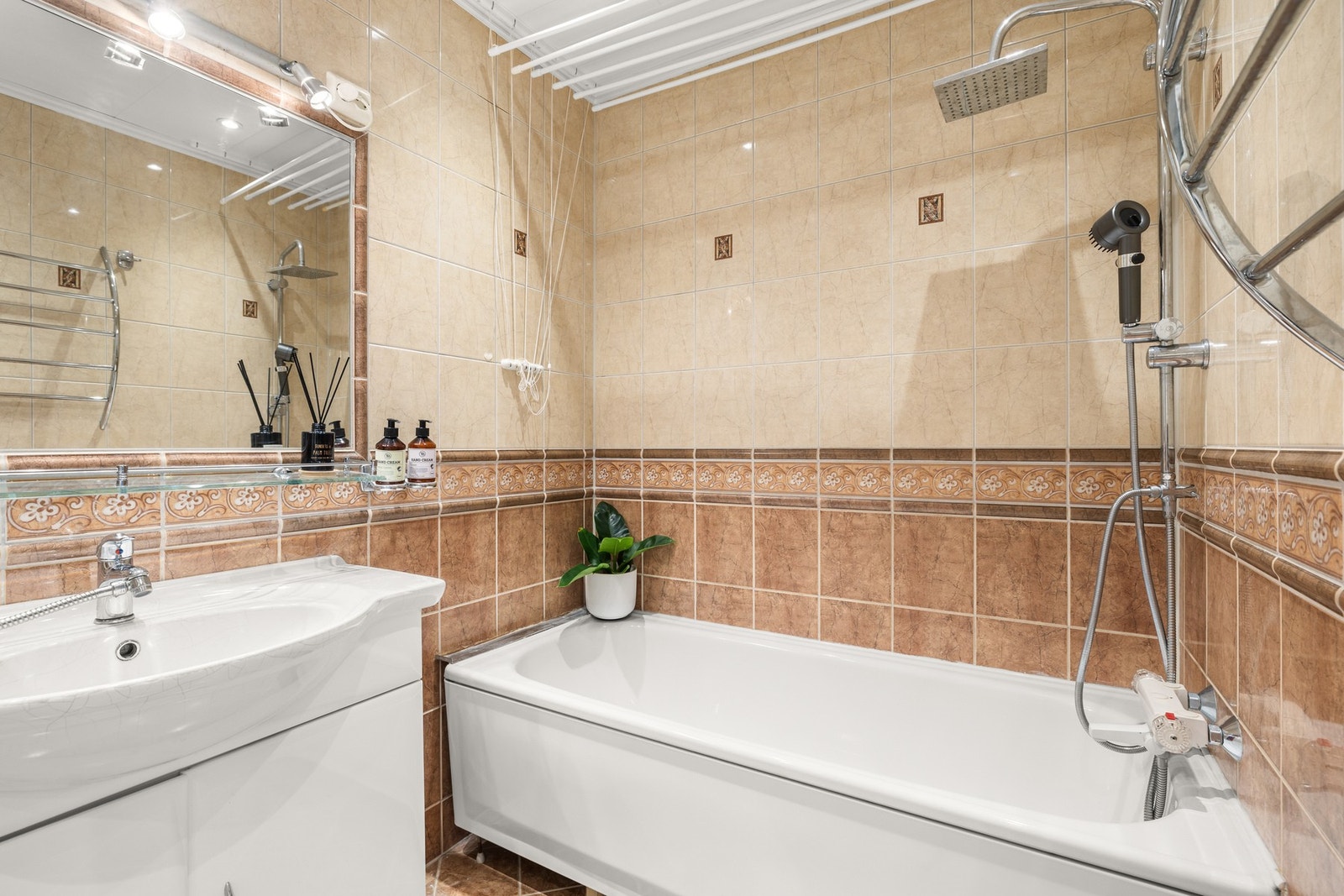 Rommet er innredet med badekar, klosett og servant med underskap, kombinert med speil med integrert belysning. Galleribilde