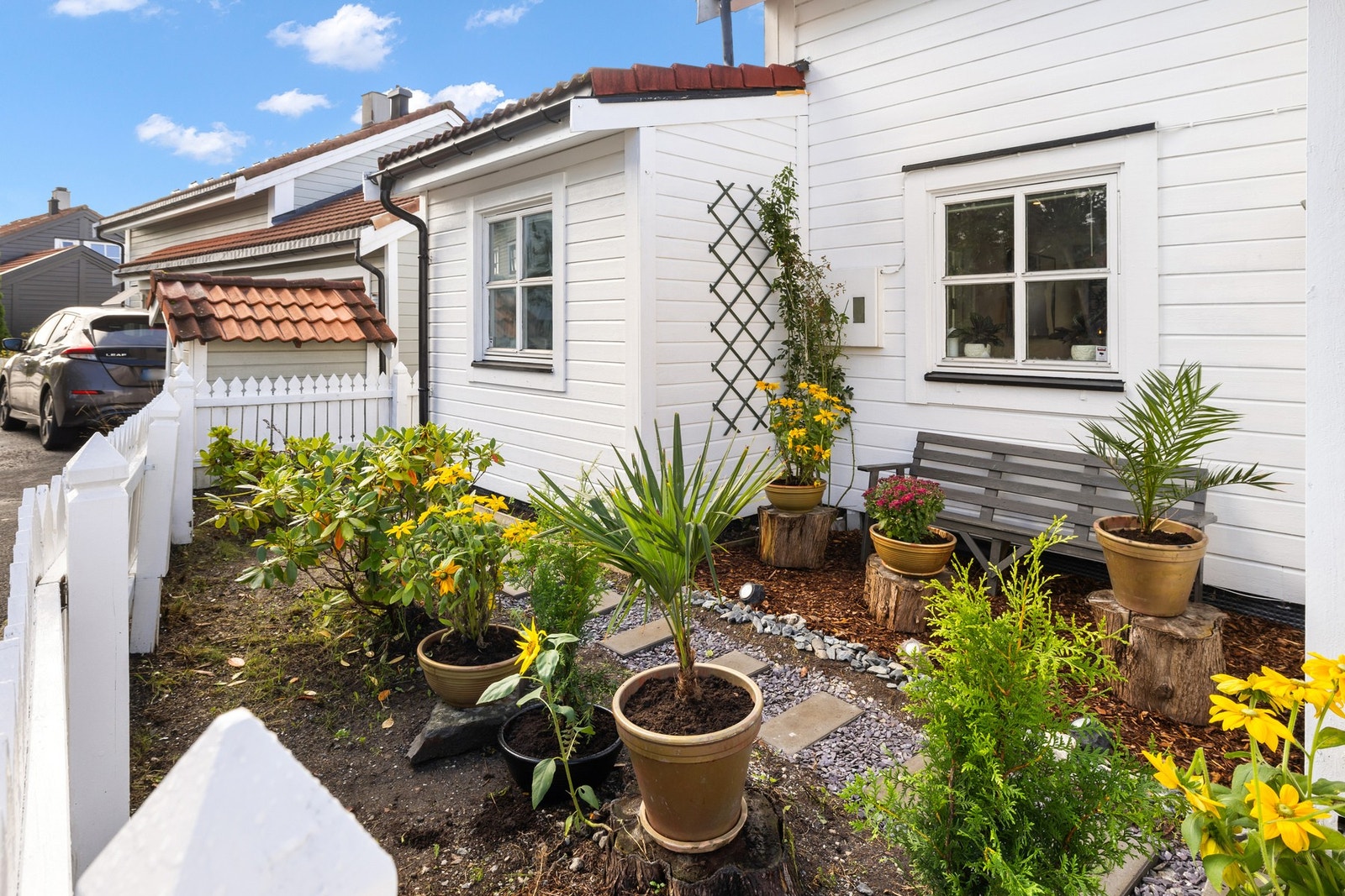 å forsiden er det et hyggelig inngangsparti med hvitmalt stakittgjerde og blomsterbed som rammer inn adkomsten. Galleribilde