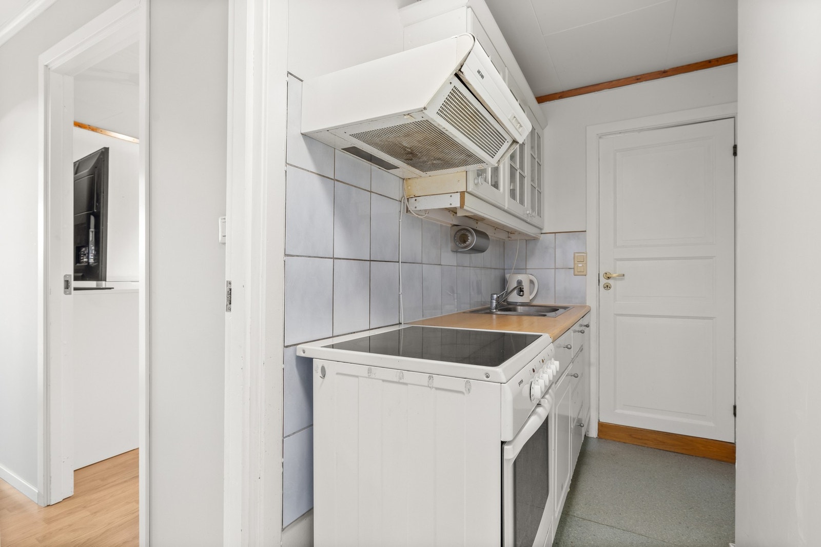 Kjøkkeninnredning med hvite profilerte fronter, overskap med fronter i glass, benkeplate i laminat, rustfri oppvaskkum og ventilator med kullfilter. Galleribilde