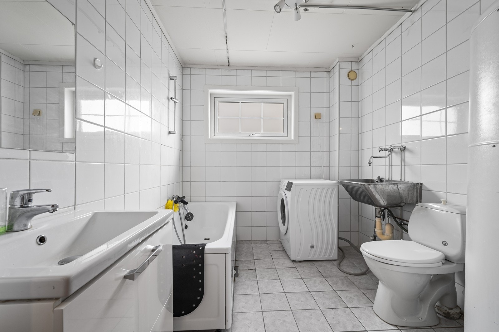 Badet er flislagt og utstyrt med badekar, toalett, servant og opplegg for vaskemaskin. Galleribilde