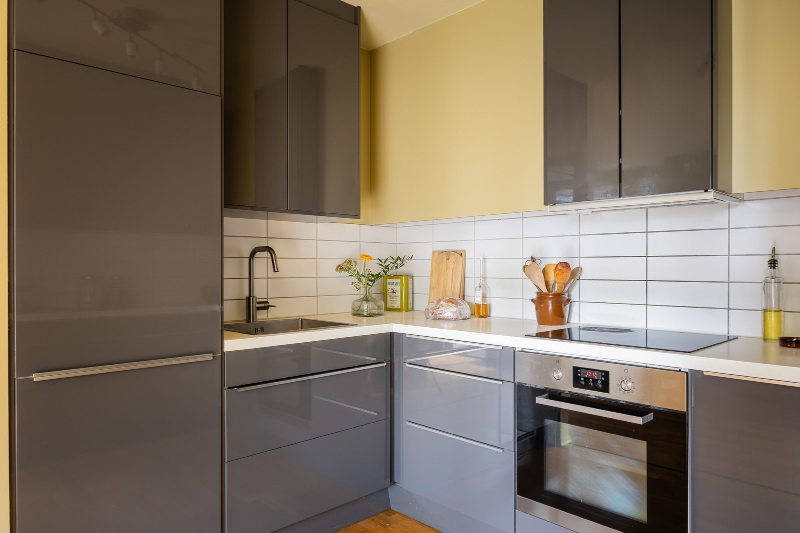 Nyere IKEA kjøkkeninnredning med glatte høyglansfronter, laminatbenkeplate, oppvaskkum, fliser over kjøkkenbenk, samt lys under overskap. Galleribilde