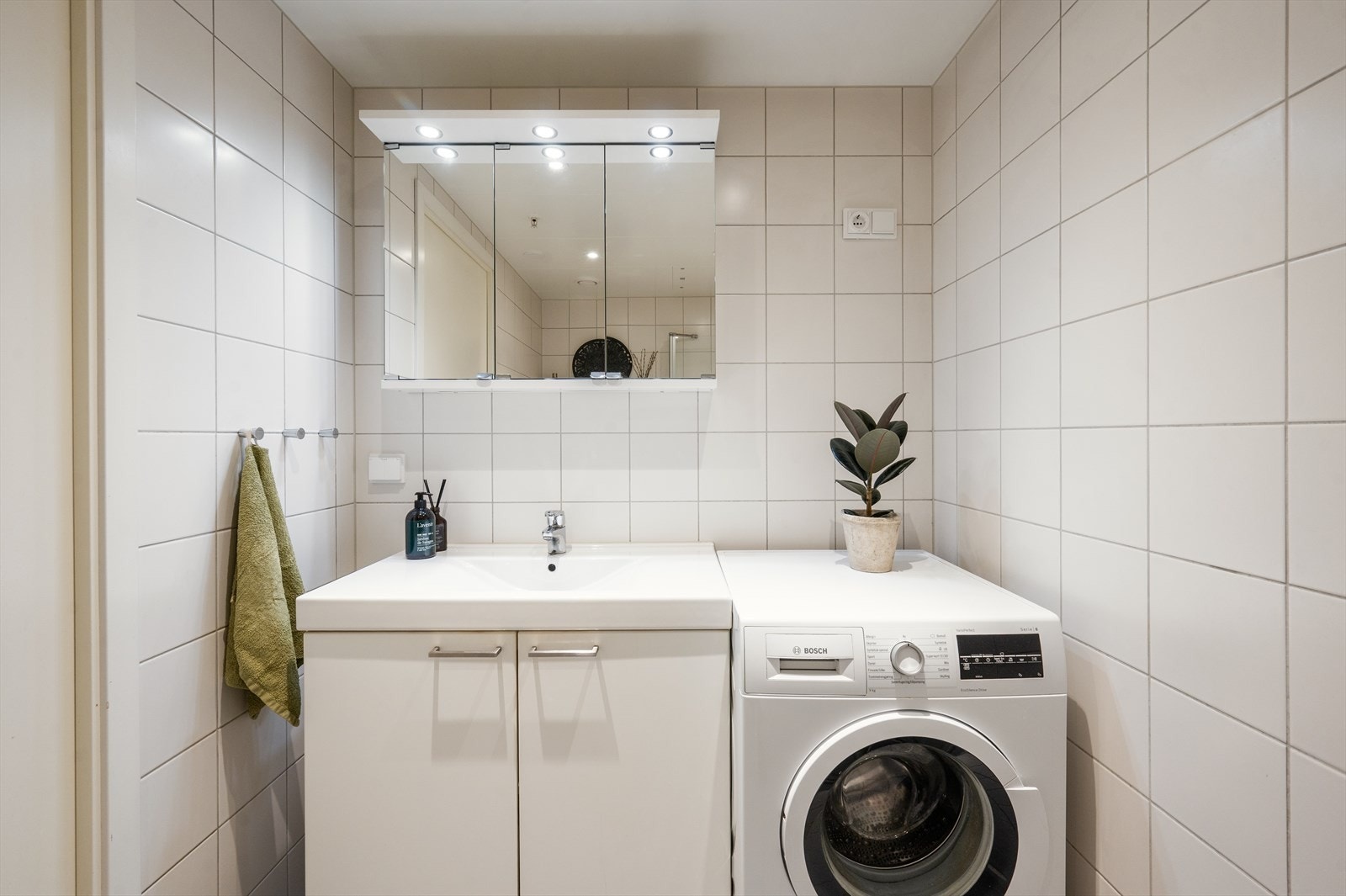 Badet er innredet med vegghengt toalett, servant med tilhørende innredning, speil med integrert lys og dusjhjørne med svingbare glassdører Galleribilde