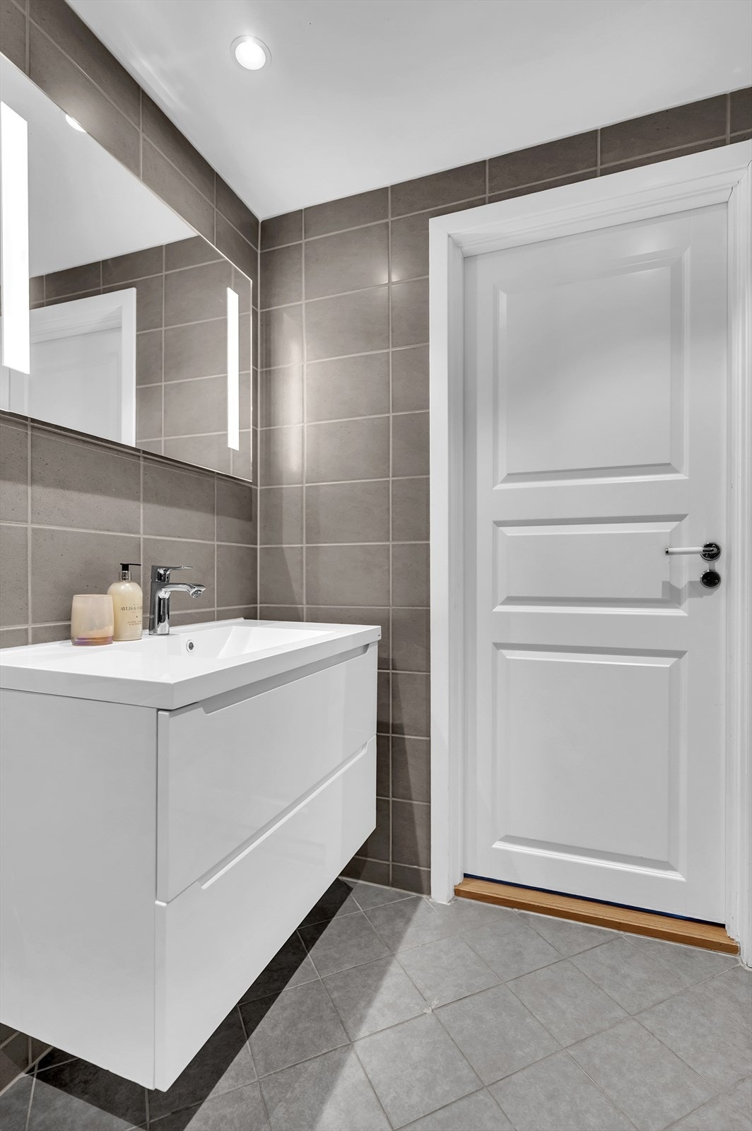 Rommet er innredet med dusj på gulv med dører i herdet glass, veggfestet klosett, opplegg for vaskemaskin og servant. Galleribilde