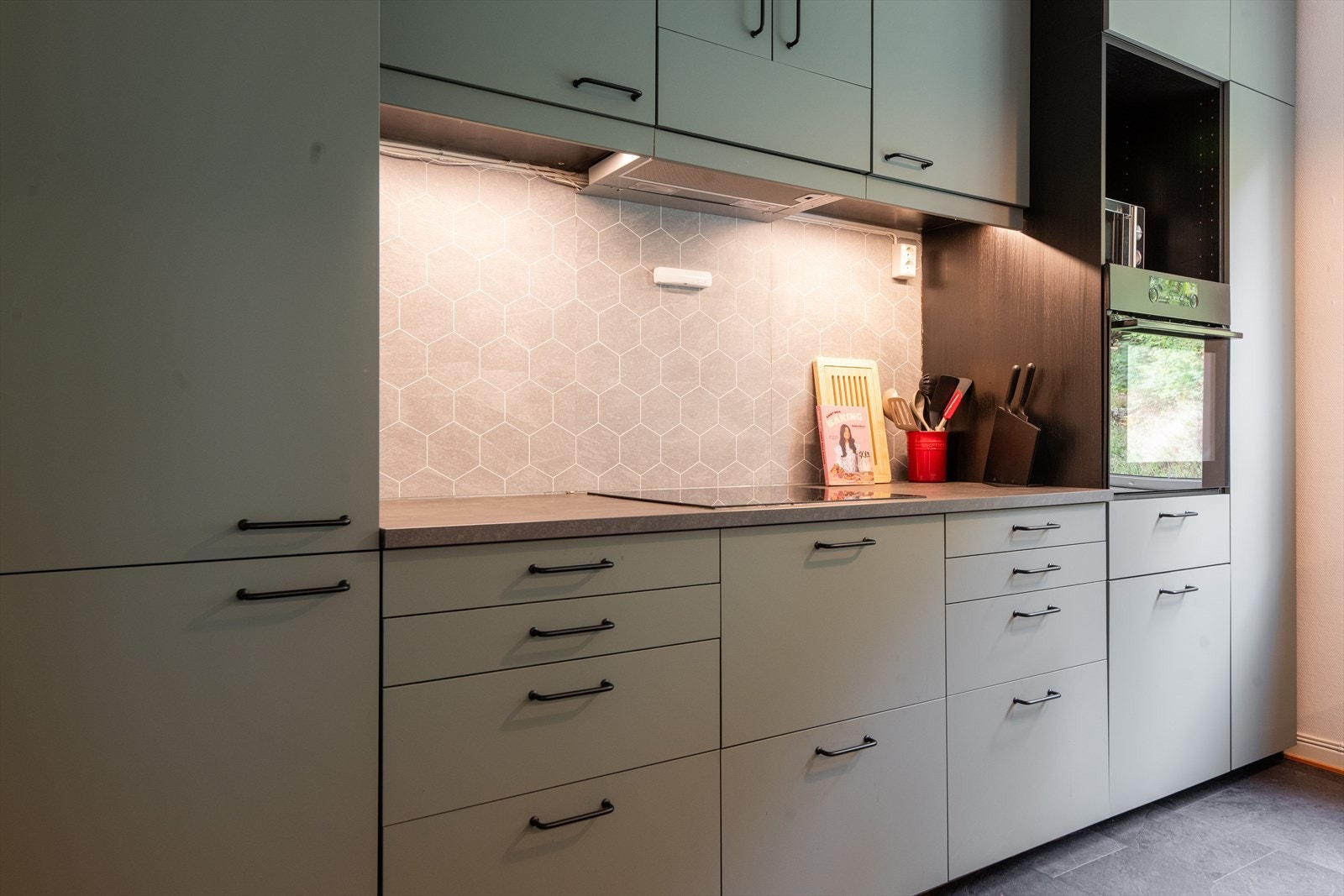 Kjøkkenet har integrerte hvitevarer som oppvaskmaskin, koketopp og kjøl/fryseskap, samt stekeovn plassert i praktisk arbeidshøyde i høyskap. Over kokesonen er det ventilator med kullfilter. Galleribilde