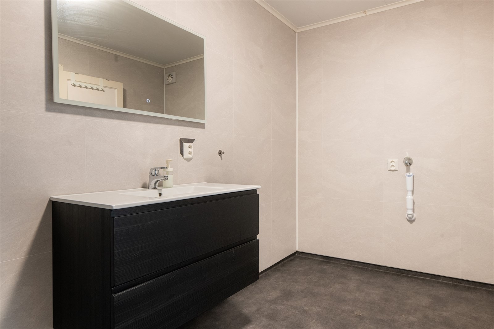 Badet er også innredet med dusjhjørne i stilrent design med sorte profiler og innfellbare glassdører. Det er også opplegg for og plass til vaskemaskin. Galleribilde