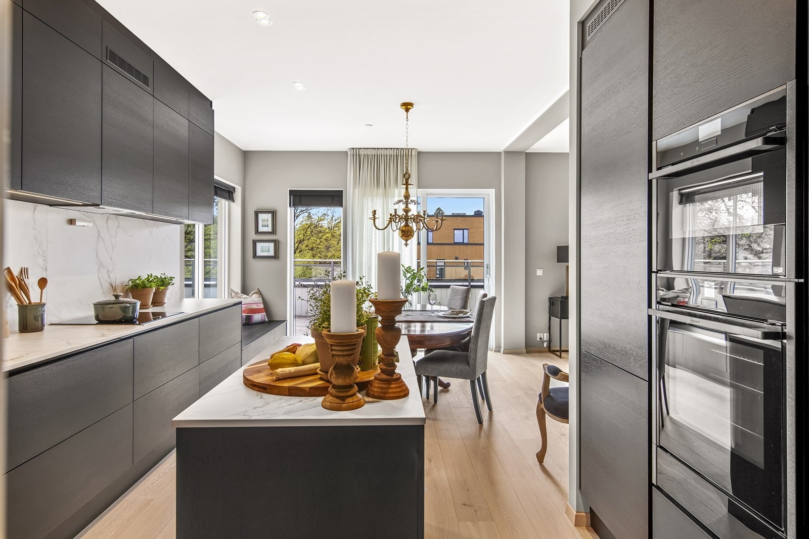 Kjøkkenet er oppgradert fra standard og er holdt i et stilrent design med stramme linjer, sorte, glatte fronter i trestruktur, matchende hyller og en tynn, lys benkeplate i marmorert corian med underlimt vaskekum. Galleribilde