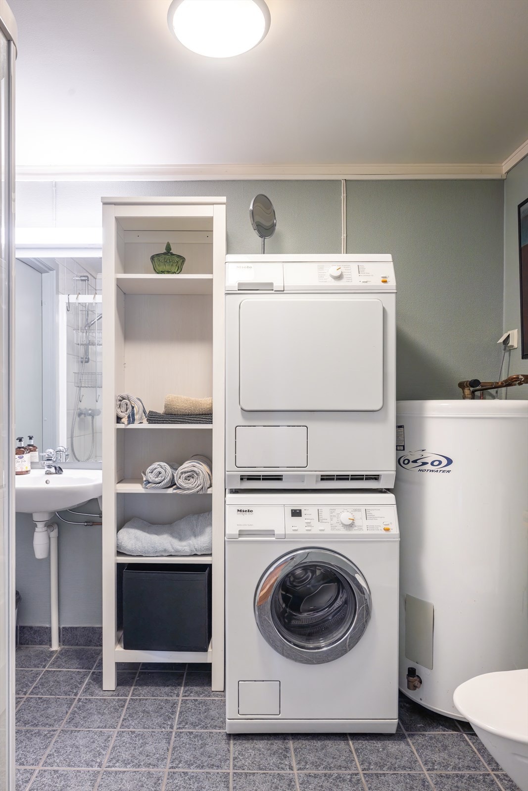 Det andre badet fungerer som kombinert vaskerom og har egen inngang til bod. Badet har mørke gulvfliser, hvite fliser i dusjhjørnet og malte, glatte vegger ellers, samt varmekabler i gulvet. Galleribilde