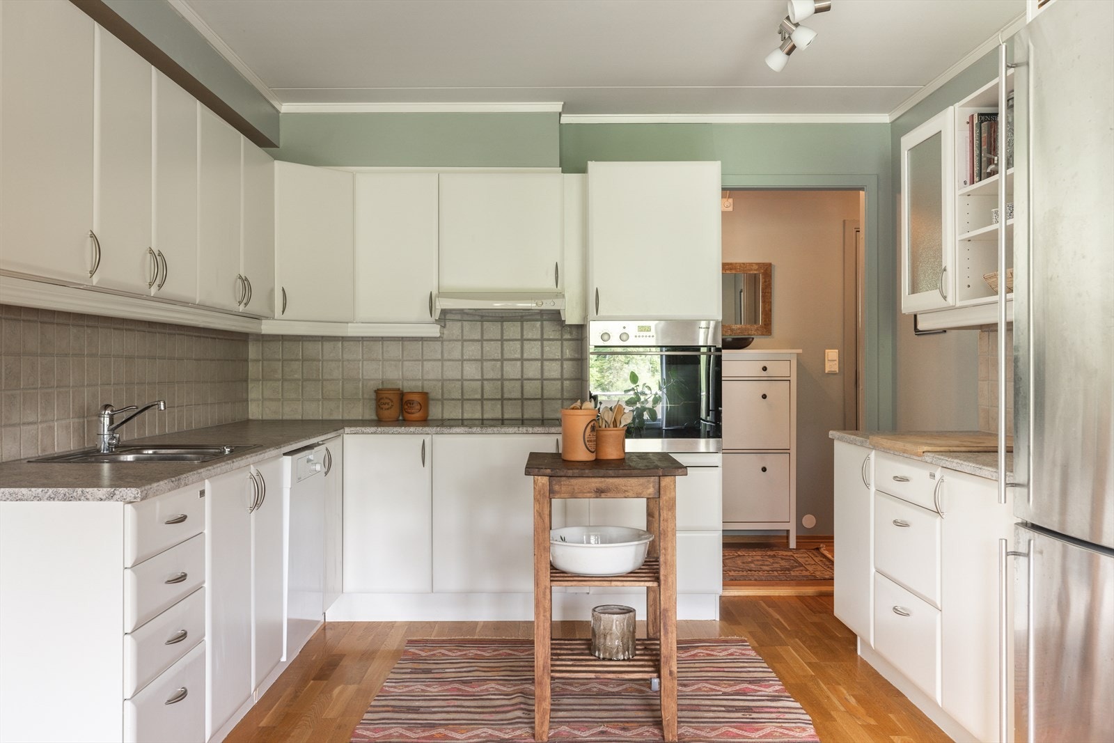 Innredningen fra Huseby er plassert langs tre sider og gir en funksjonell arbeidsflyt med godt med skap- og benkeplass. De lyse frontene er kombinert med to vitrineskap og benkeplate i grå laminat med nedfelt stålvask. Galleribilde