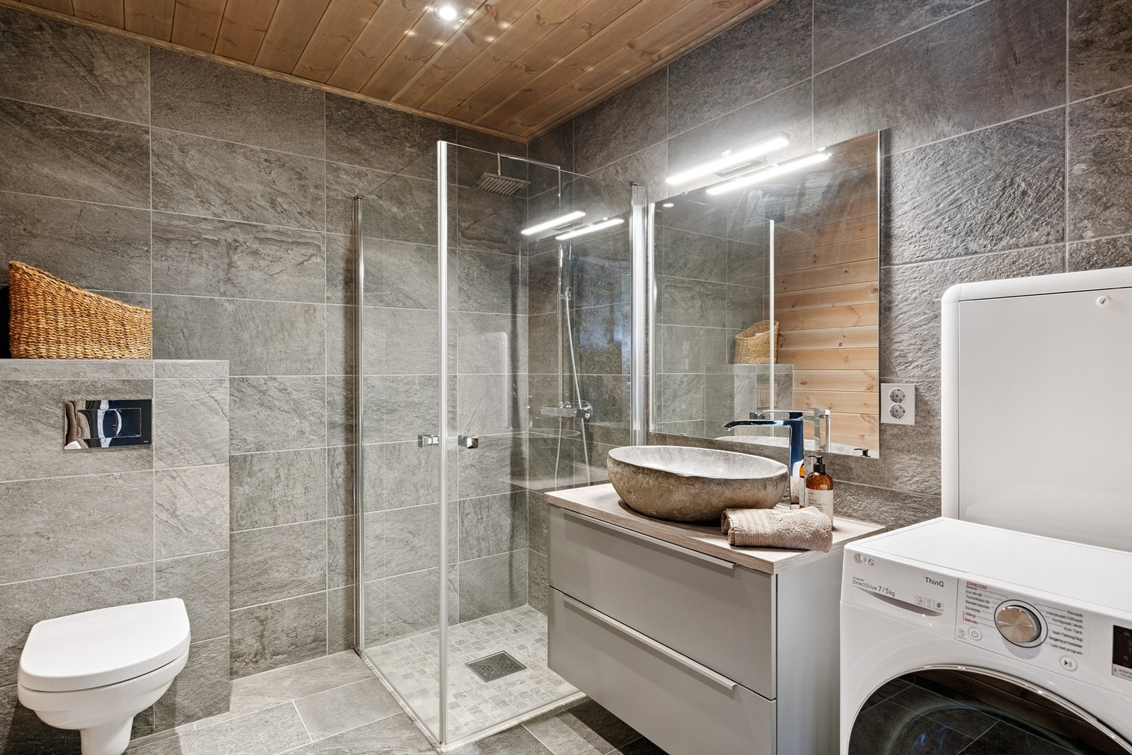 Denne leiligheten har flislagt to vegger, trepanel på resterende vegger. Vegghengt toalett, innredning med stilig servant plassert på benk. Det er opplegg for vaskemaskin Galleribilde