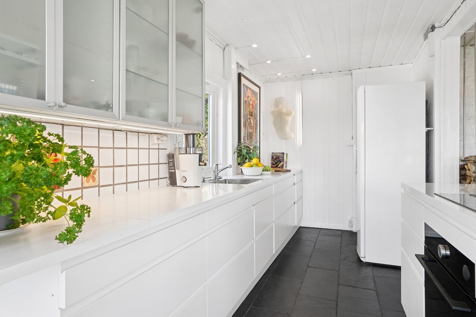 Kjøkkenet er utstyrt med hvit kjøkkeninnredning, laminat benkeplate, fliser over benk, utslagsvask med blandebatteri og opplegg for oppvaskmaskin. Lys under overskap. Stedvise overskapfronter med glass. Avsatt plass til kjøl/frys. Komfyrvakt. Galleribilde