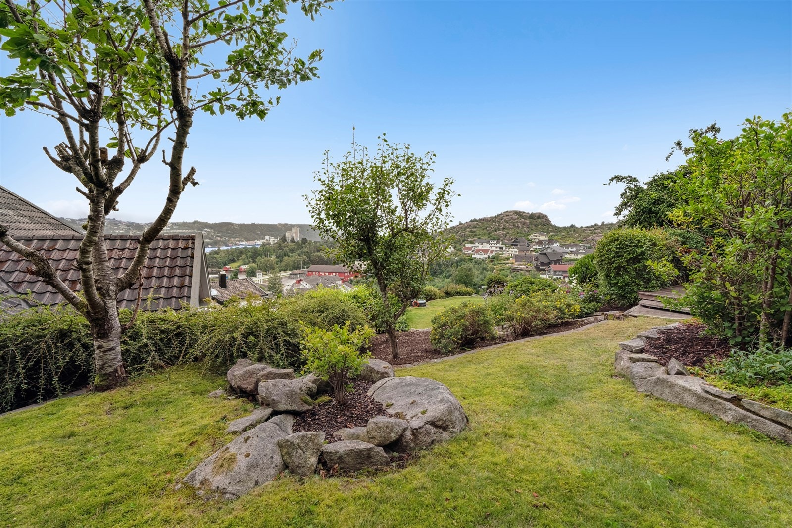 Stor del av tomten er naturtomt. Resten er pent opparbeidet hage med gruslagte stier, sitteområder, busker og trær. Galleribilde