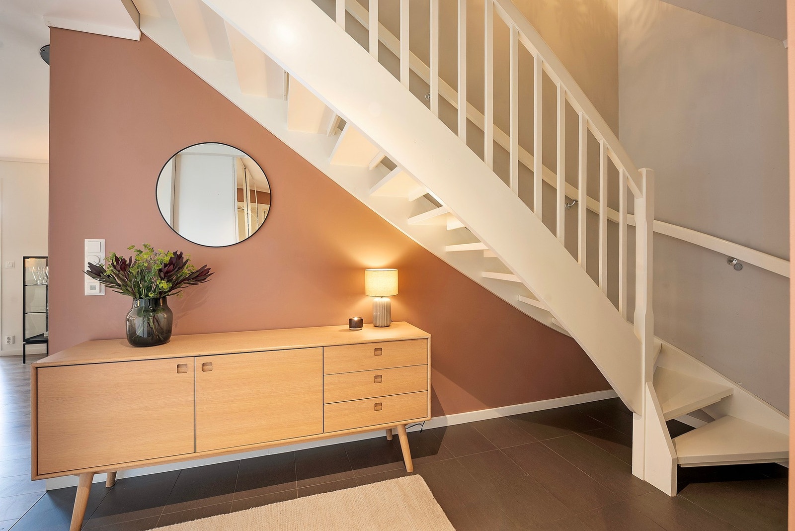 Entréen er malt i lune og behagelige toner som fremhever den lyse trappen, mens de mørke flisene skaper en elegant kontrast og et helhetlig førsteinntrykk Galleribilde