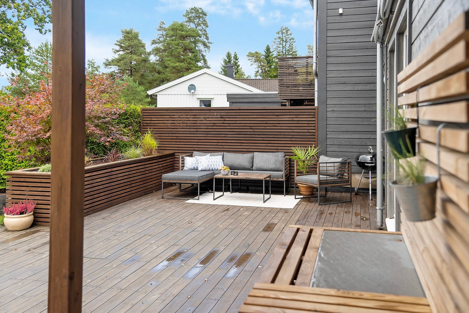 Utvendig finner du et koselig terrasseområde som leder deg videre ned i hagen - her skaper den plassbygde blomsterkassen en lun og intim følelse på den åpne flaten Galleribilde