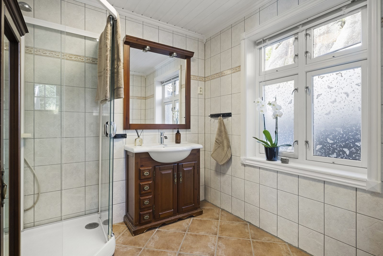 Romslig baderom med lyse fliser på vegger og gulv, med varmekabler Galleribilde