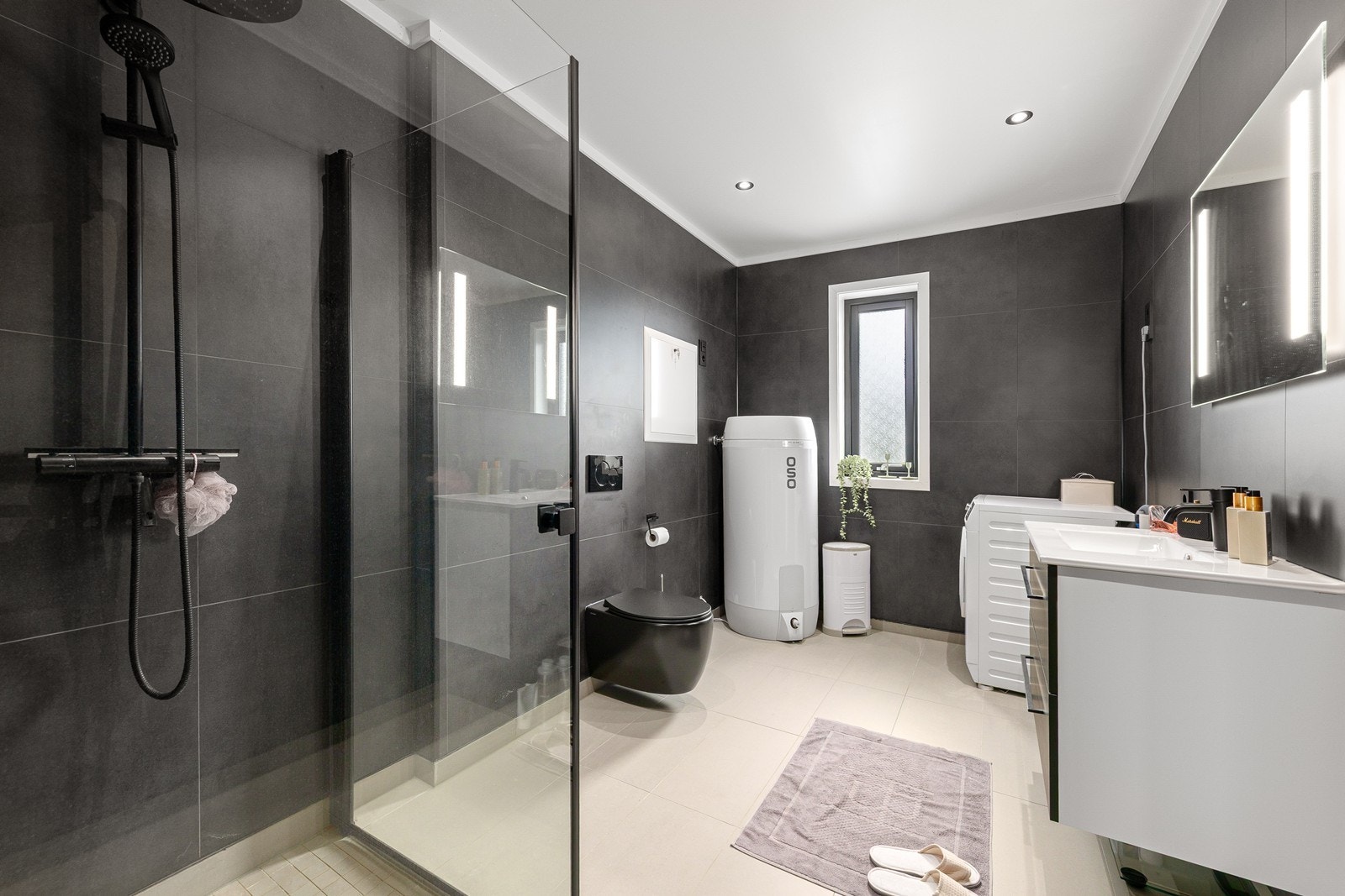 Delikat baderom med varmekabler. Badet inneholder dusjhjørne med dusjvegger, servantinnredning med speil, vegghengt toalett og opplegg for vaskemaskin. Galleribilde