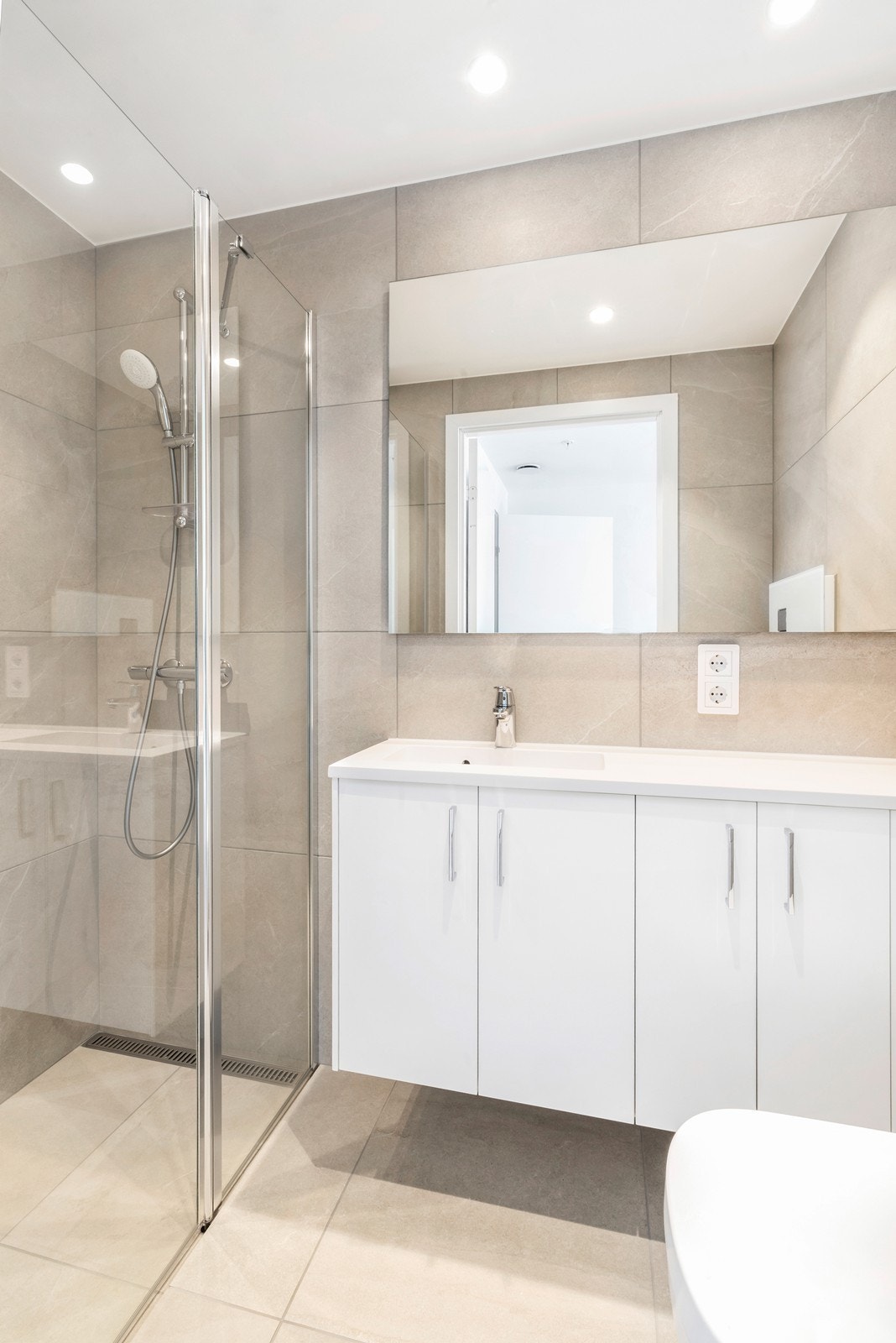 Badet har fliser på vegger og gulv. Dusj og vegghengt toalett. Galleribilde