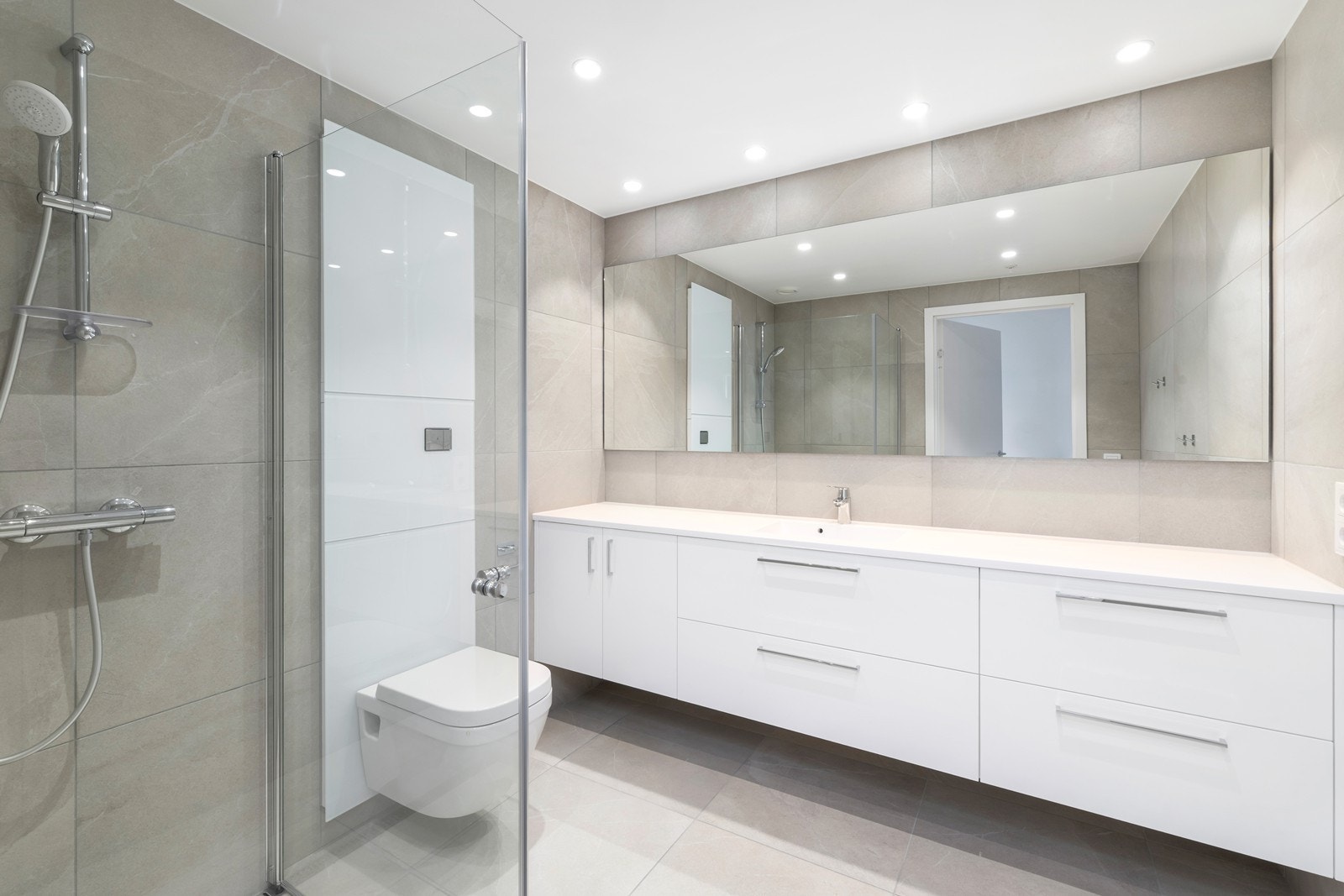 Flislagt bad med dusjhjørne, servant og vegghengt toalett. Galleribilde