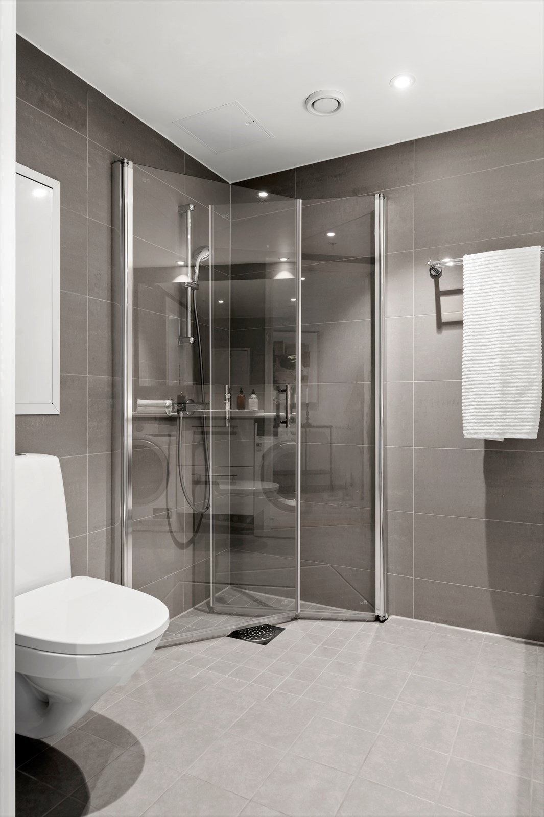 Badet er utstyrt med dusjhjørne med innfellbare dører, servant med oppbevaring, vegghengt toalett og opplegg for vaskemaskin. Galleribilde