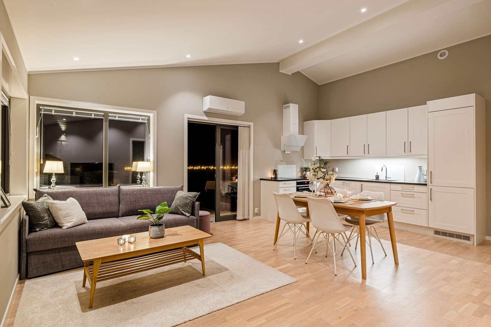 Et oppholdsrom som både er praktisk og elegant - med varme fra vedovn, lys fra store vinduer og en funksjonell kjøkkenløsning. Galleribilde