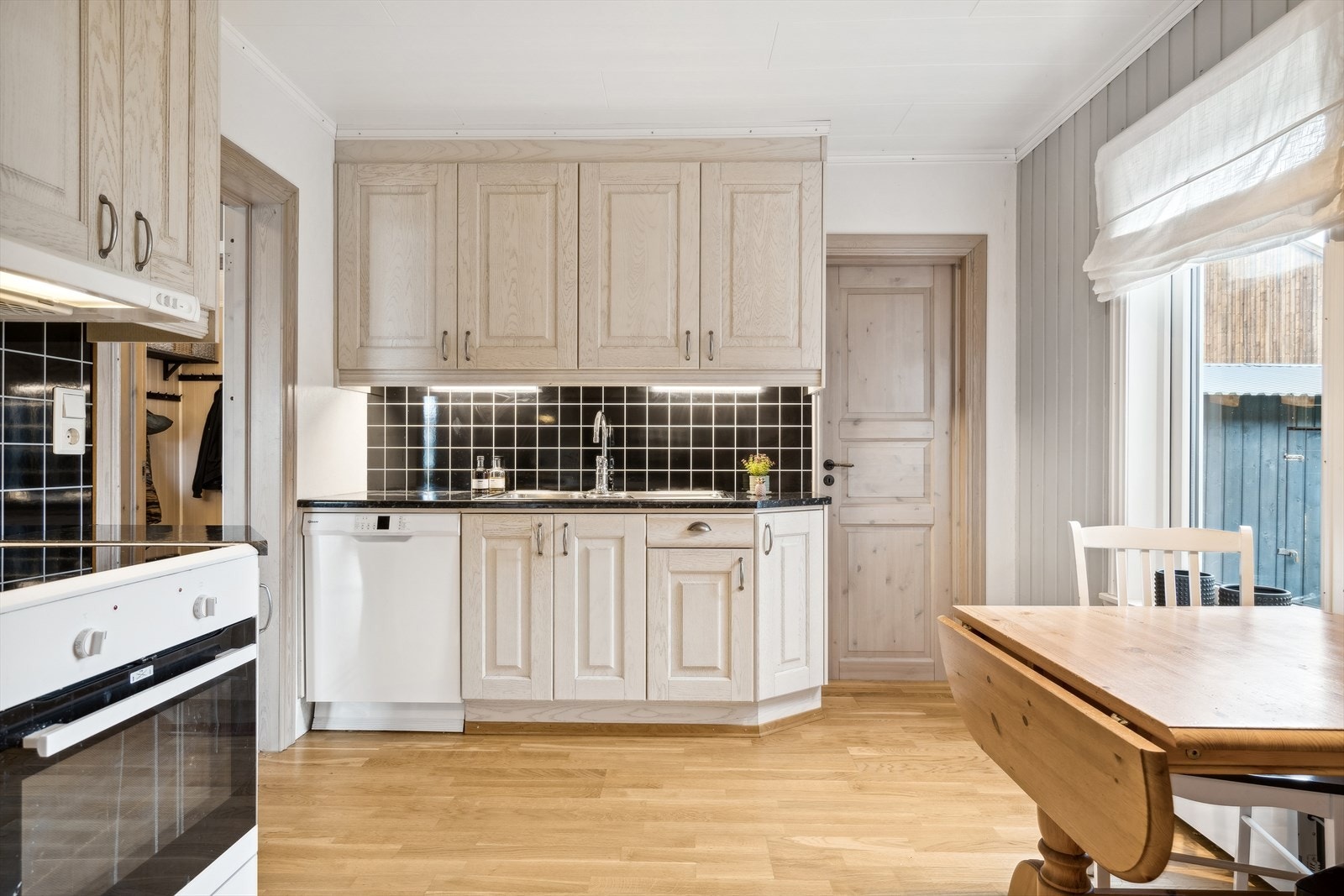 Kjøkkenet er separat og har en stilren innredning med lyse profilerte fronter, laminat benkeplate med nedfelt vask og Kitchenboard på vegg over benk Galleribilde