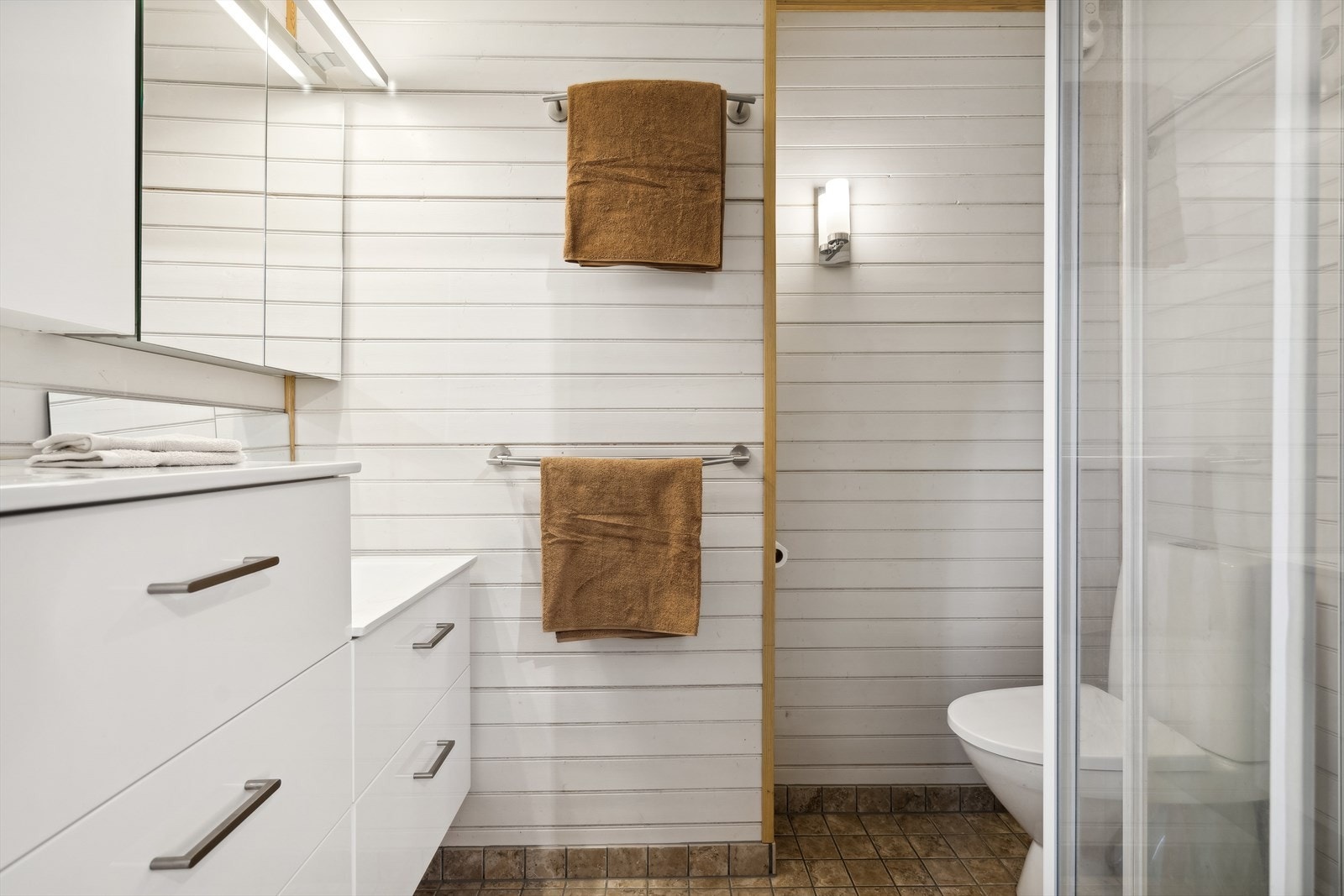 Badet er utført med flislagt gulv m/varmekabler og panelvegger - Her finner du toalett, dusjkabinett og baderomsinnredning med flere skuffer/skap Galleribilde