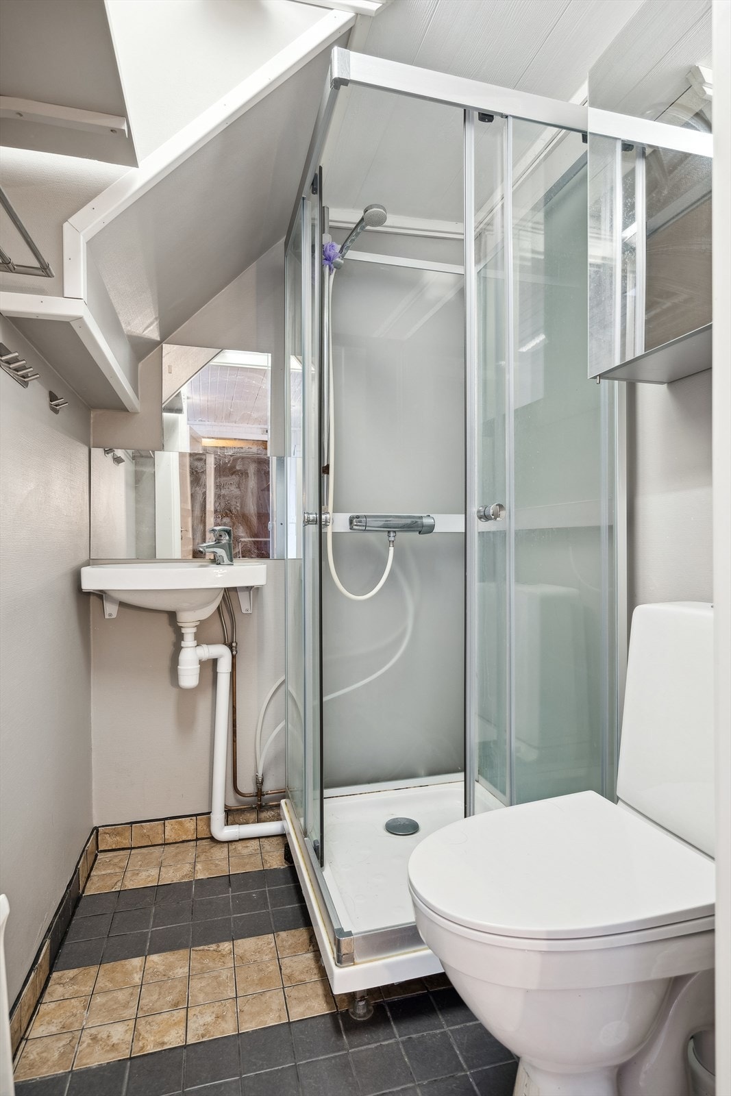 Badet har flislagt gulv med sokkelfliser og våtromsstrie på vegger - Her finner du toalett, dusjkabinett og servant Galleribilde