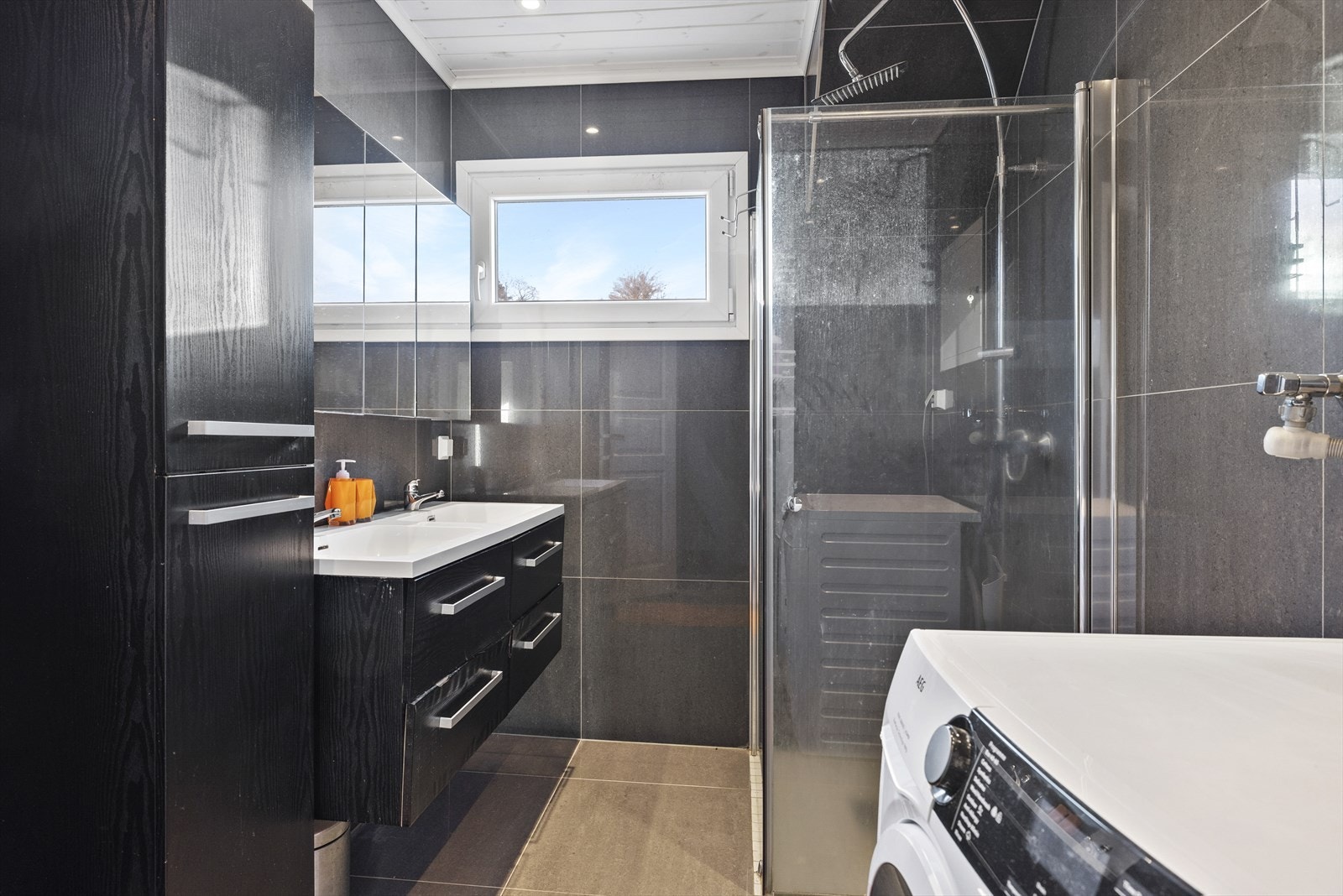 Baderom som ble pusset opp i 2018/2019. Badet er innredet med benkeskap og høyskap med glatte fronter, veggskap med speilfronter over servant, dusj med innfellbare dører i herdet glass, dobbel servant i helstøpt plate og opplegg for vaskemaskin. Galleribilde