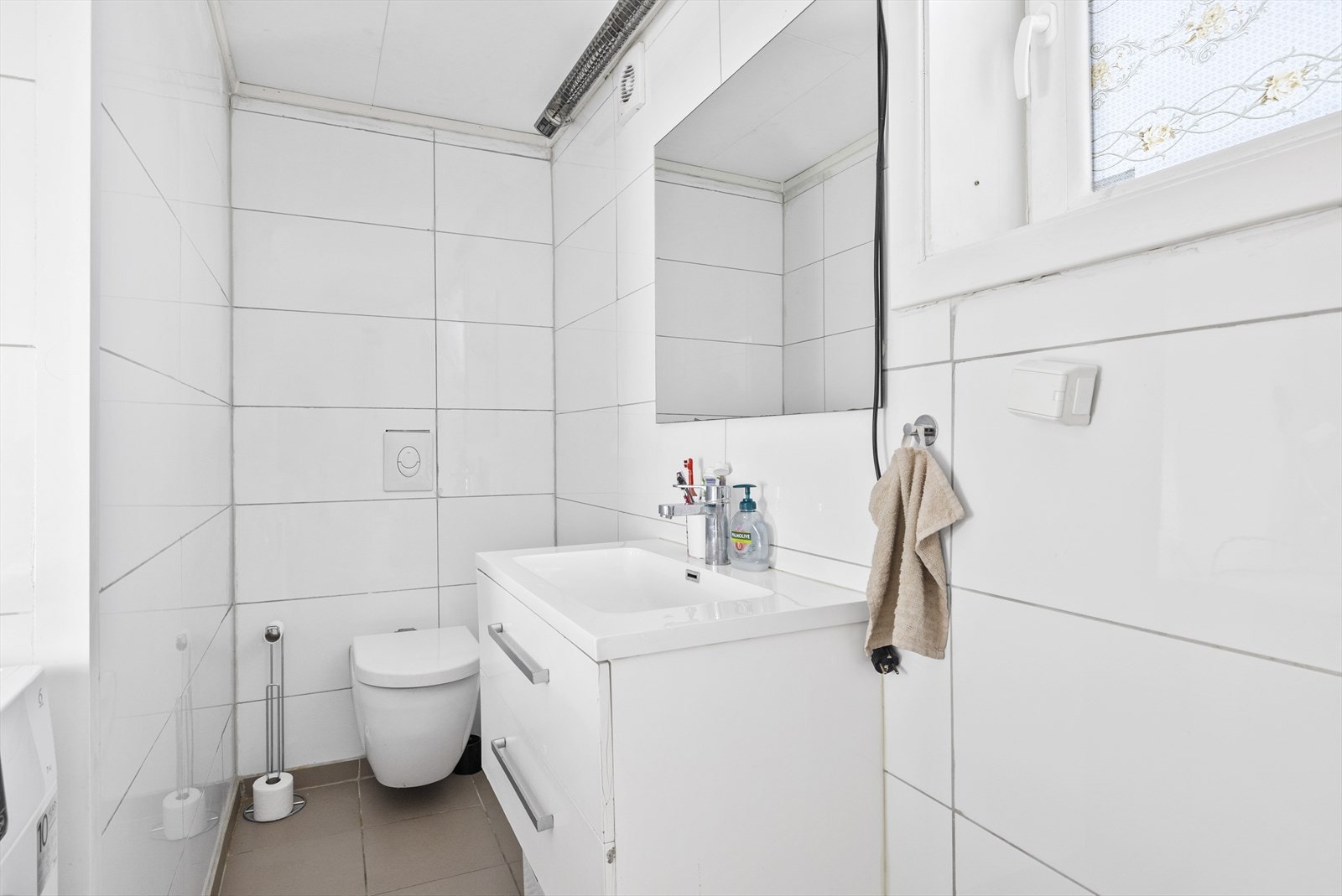 Flislagt baderom med benkeskap med glatte fronter, dusj på gulv, servant i helstøpt plate, veggfestet klosett med innebygget sisterne og opplegg for vaskemaskin. Galleribilde