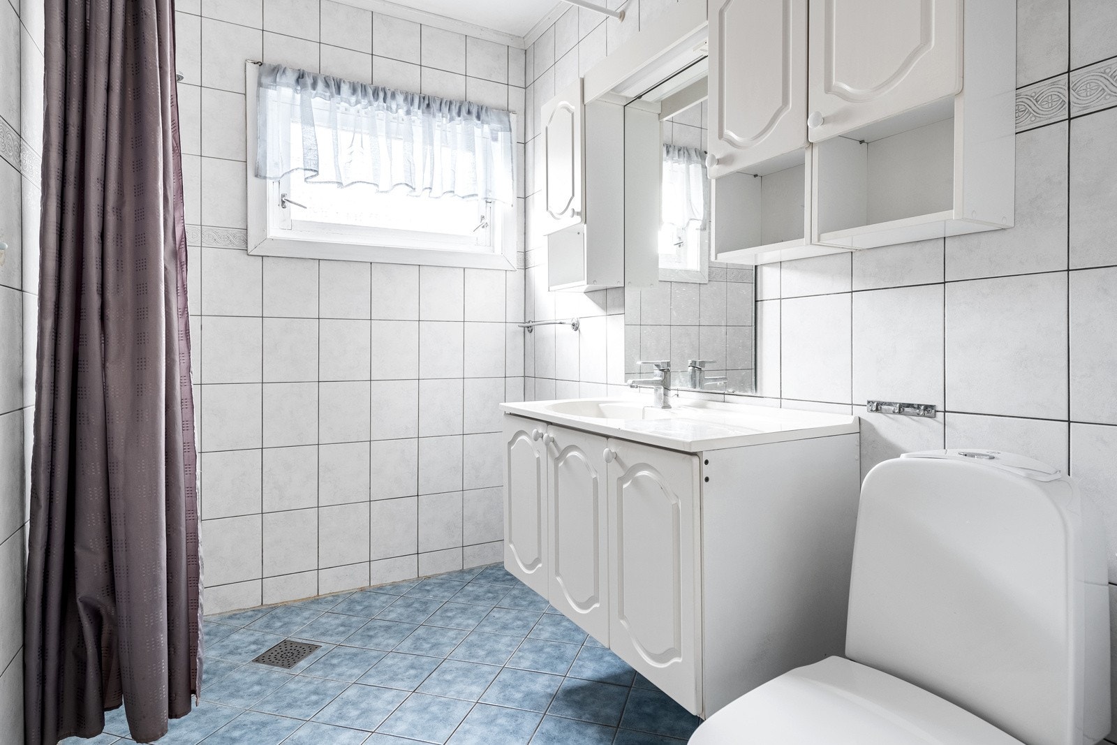 Baderom med lyse fliser og hvit innredning. Toalett, dusj og godt med skapinnredning Galleribilde