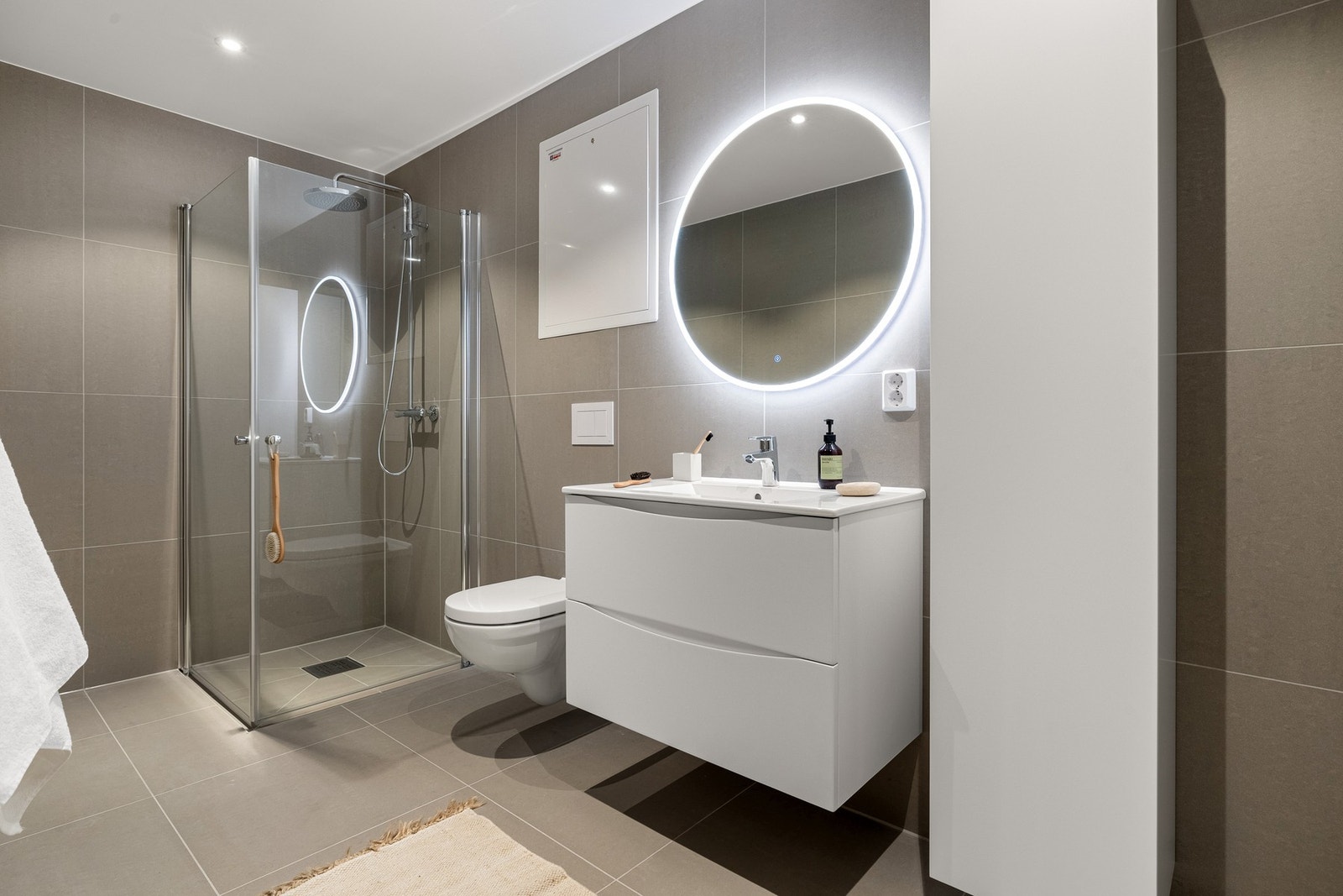 Det er innredet med et vegghengt toalett, dusjhjørne med vegger og baderomsmøblement med høyskap, speil og belysning. Galleribilde