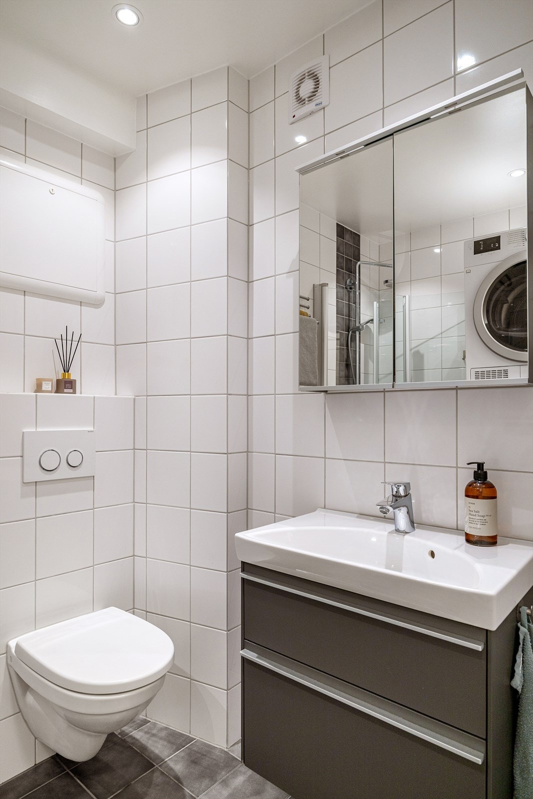 Badet er innredet med benkeskap med servant, dusjdører i glass, vegghengt toalett og opplegg for vaskemaskin. Galleribilde