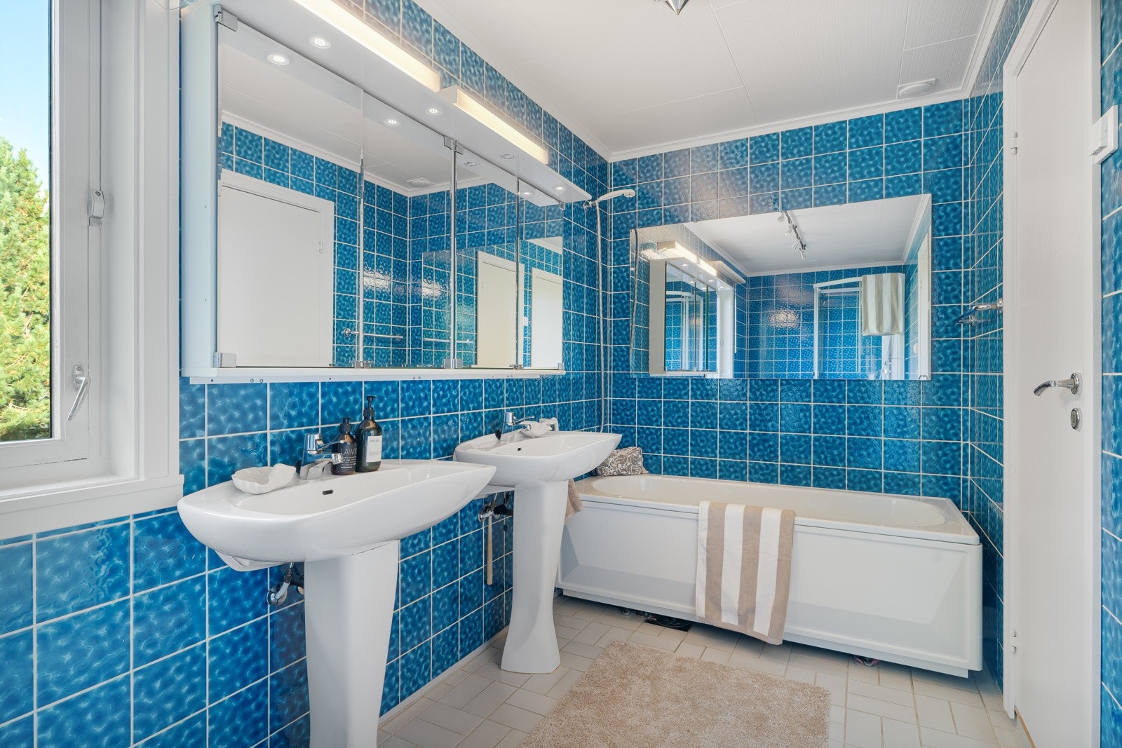 Det flislagte badet på 8 kvm fremstår funksjonellt og innbydende, med dusj, toalett, badekar, to servanter og speilskap. Galleribilde