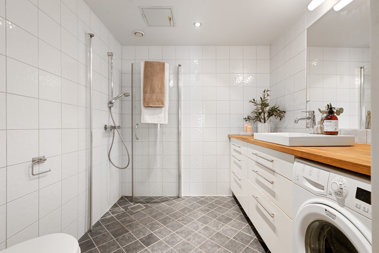 Tidløst og flislagt bad med god plass. Badet er innredet med innfellbare dusjdører, veggmontert wc og servantskap med ett greps blandebatteri fra Grohe. Galleribilde