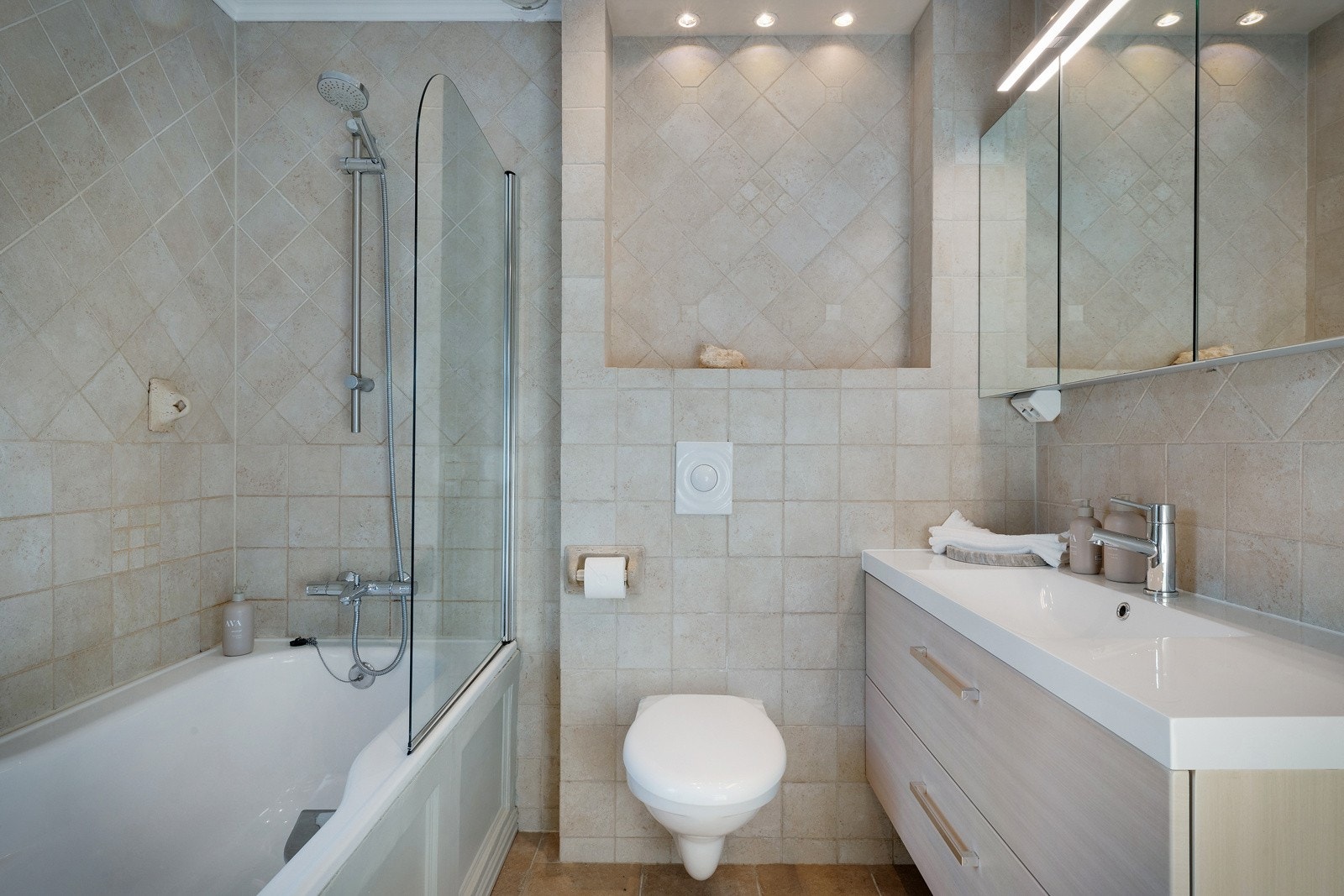 Badet er innredet med badekar, vegghengt toalett, servant med underskap og speil med belysning. Galleribilde