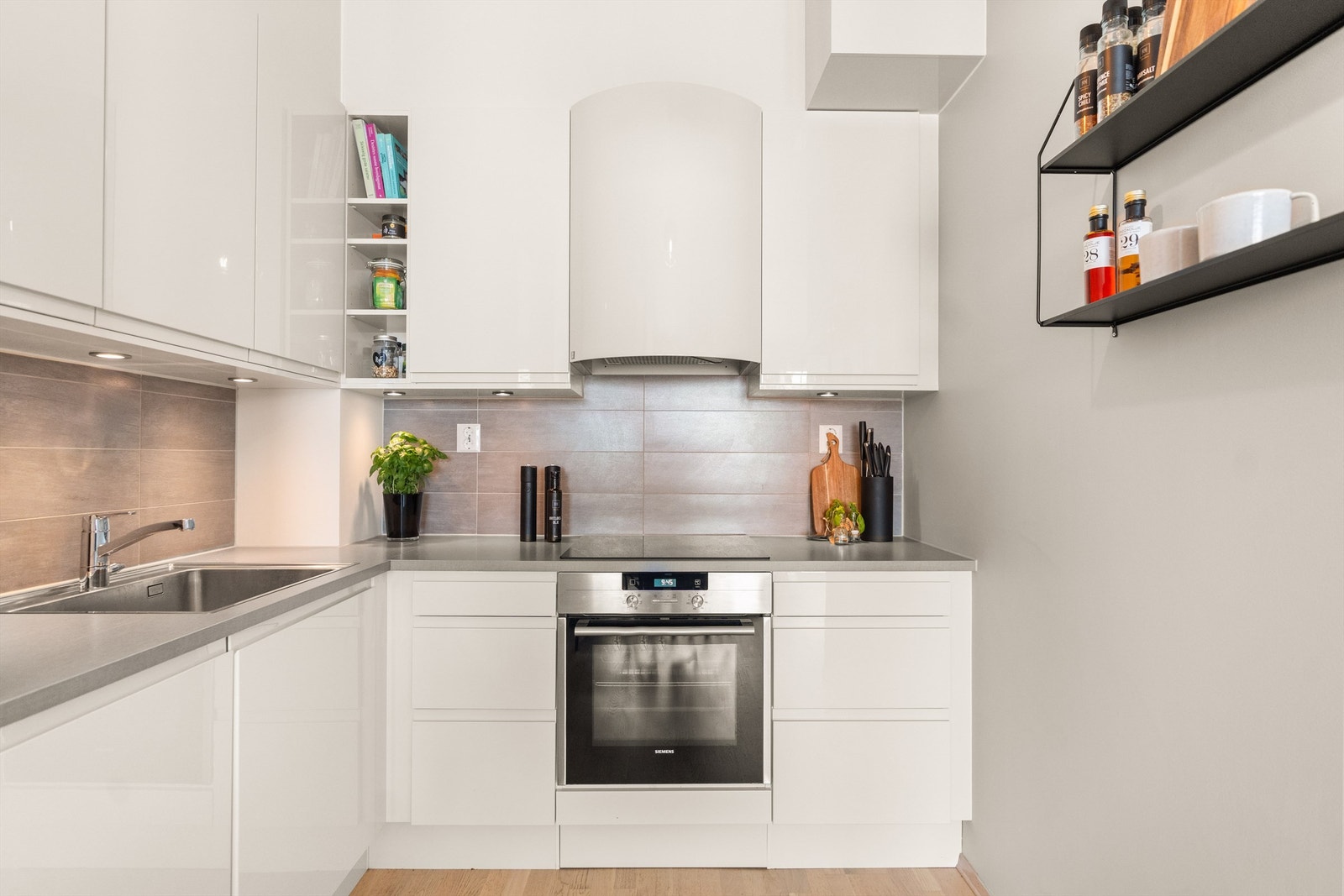 Det er fliser mellom benk og overskap og downlights under skapene. "Røroshetta" ventilasjonshette over koketoppen, sees midt i bildet. Alle hvitevarer i kjøkkenet følger med Galleribilde