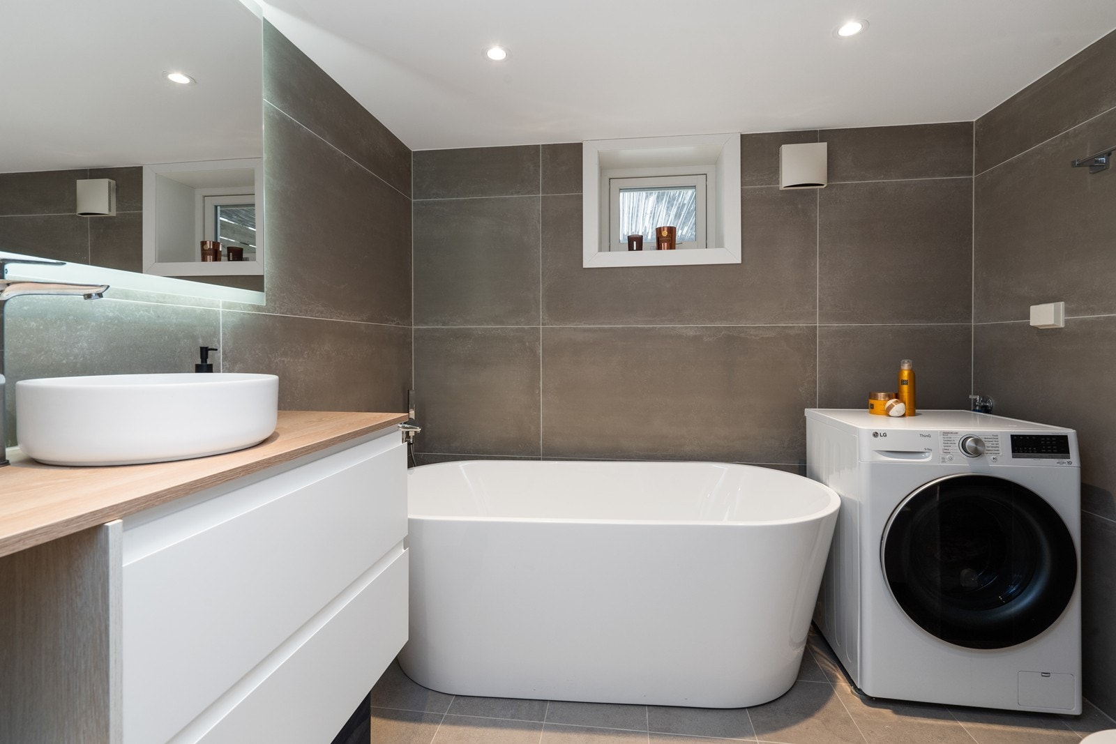 Kjellerbad med moderne innredning, romslig badekar og opplegg for vaskemaskin. Det er varmekabler i gulvet. Galleribilde