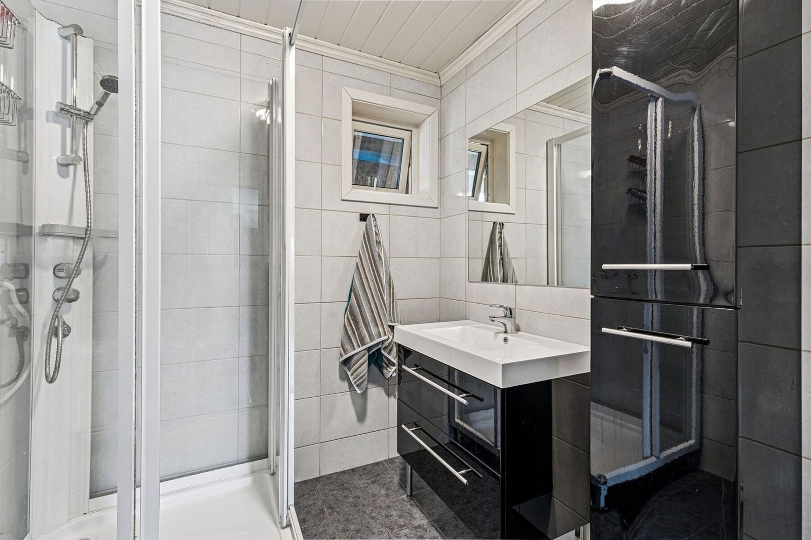 Rommet har dusjkabinett, vegghengt servant med moderne innredning og speil, samt vegghengt høyskap som gir god oppbevaringsplass. Galleribilde