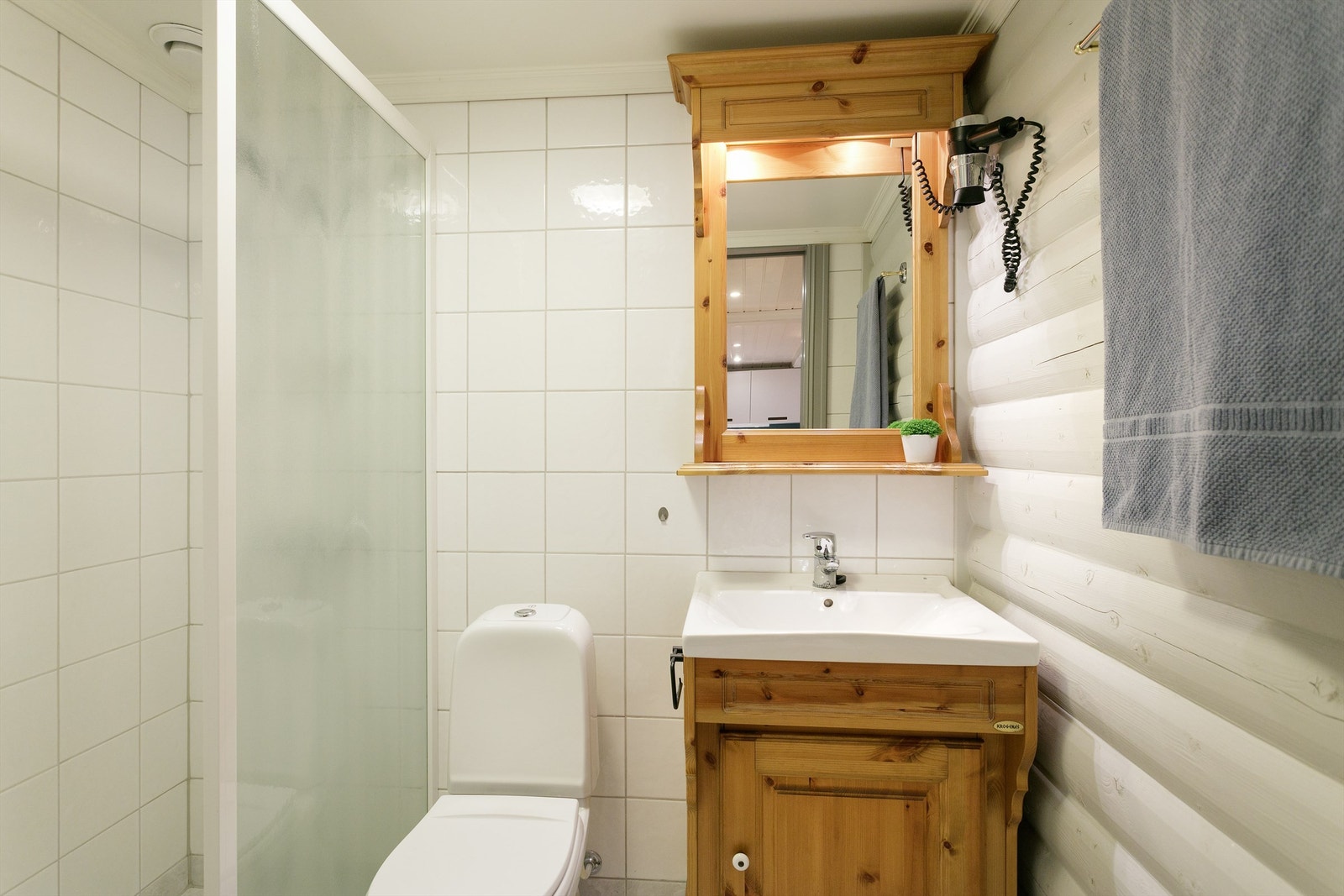 Bad har flislagt gulv med gulvvarme, malte tømmervegger, fliser på vegg i dusjsone. Wc, dusjvegg og innredning med servant. Galleribilde