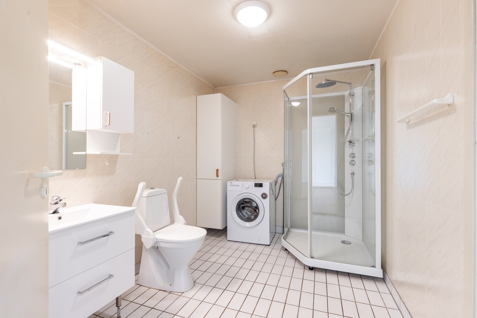 Badet er innredet med toalett, dusjkabinett og servantinnredning med skuffer, overskap og speil med overlys. Det er opplegg for vaskemaskin. Galleribilde